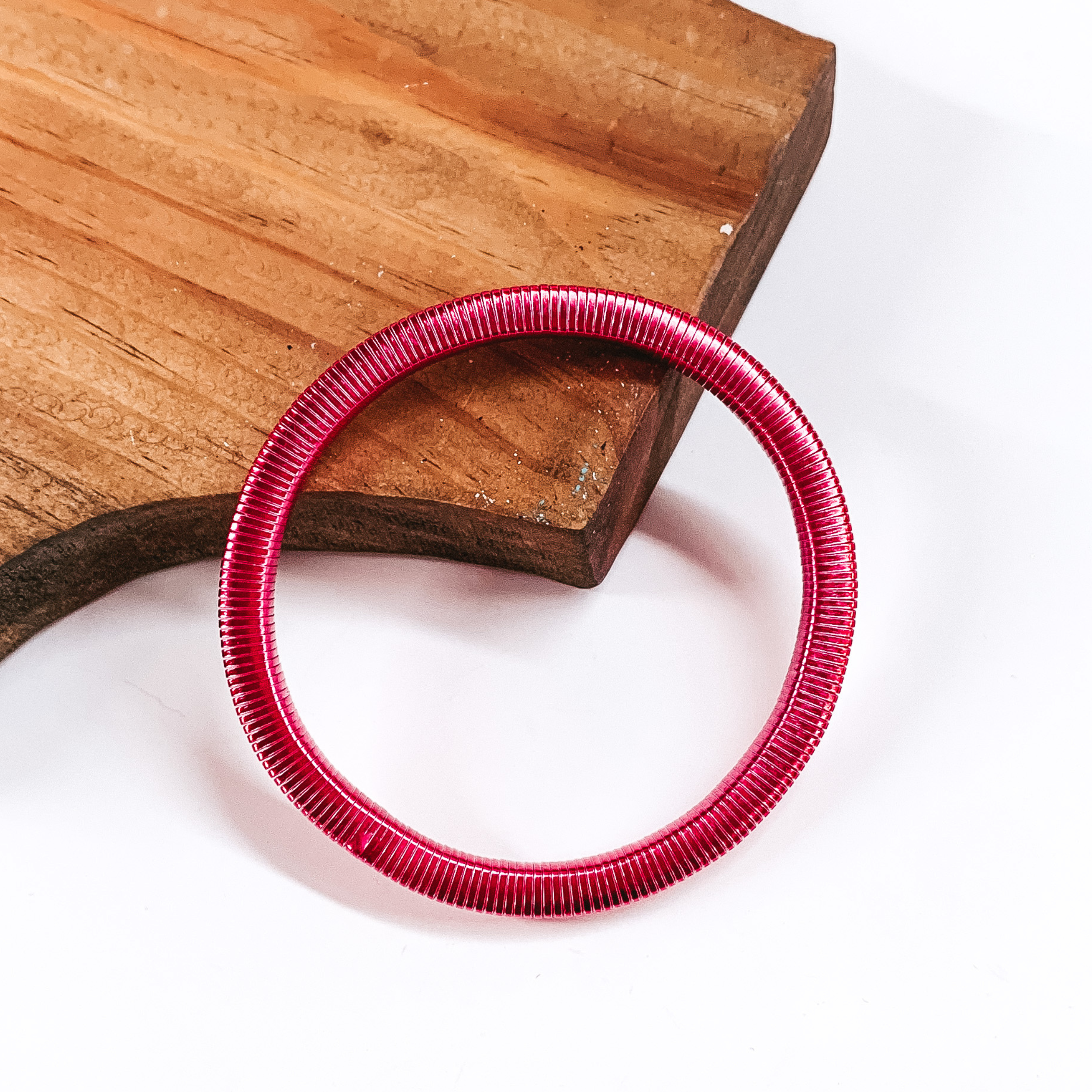 This is a hot pink Herringbone bracelet. It is partially laying on a wooden board, on a white background.
