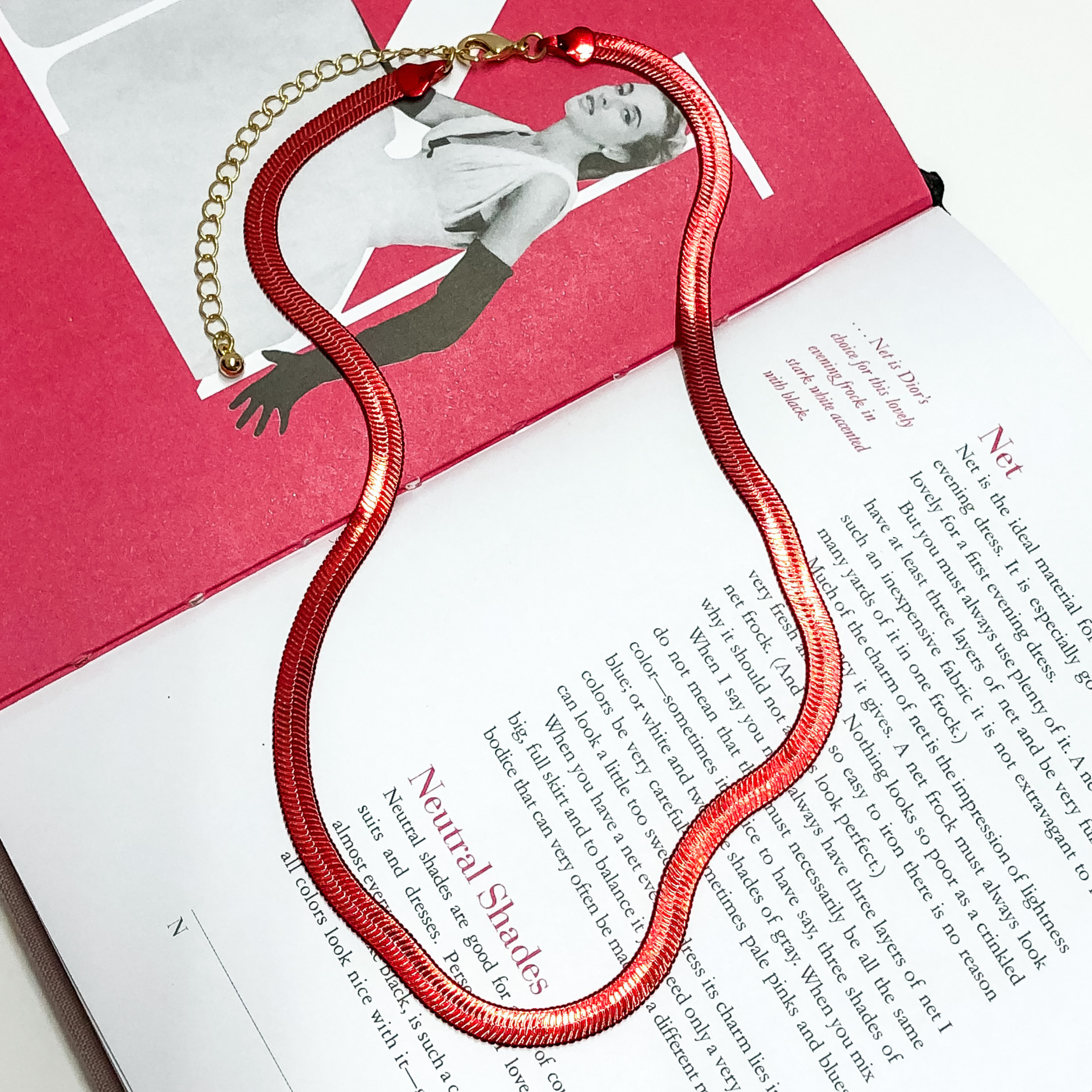 Red Herringbone chain with a gold extender. This necklace is on a opened book, on a white background.