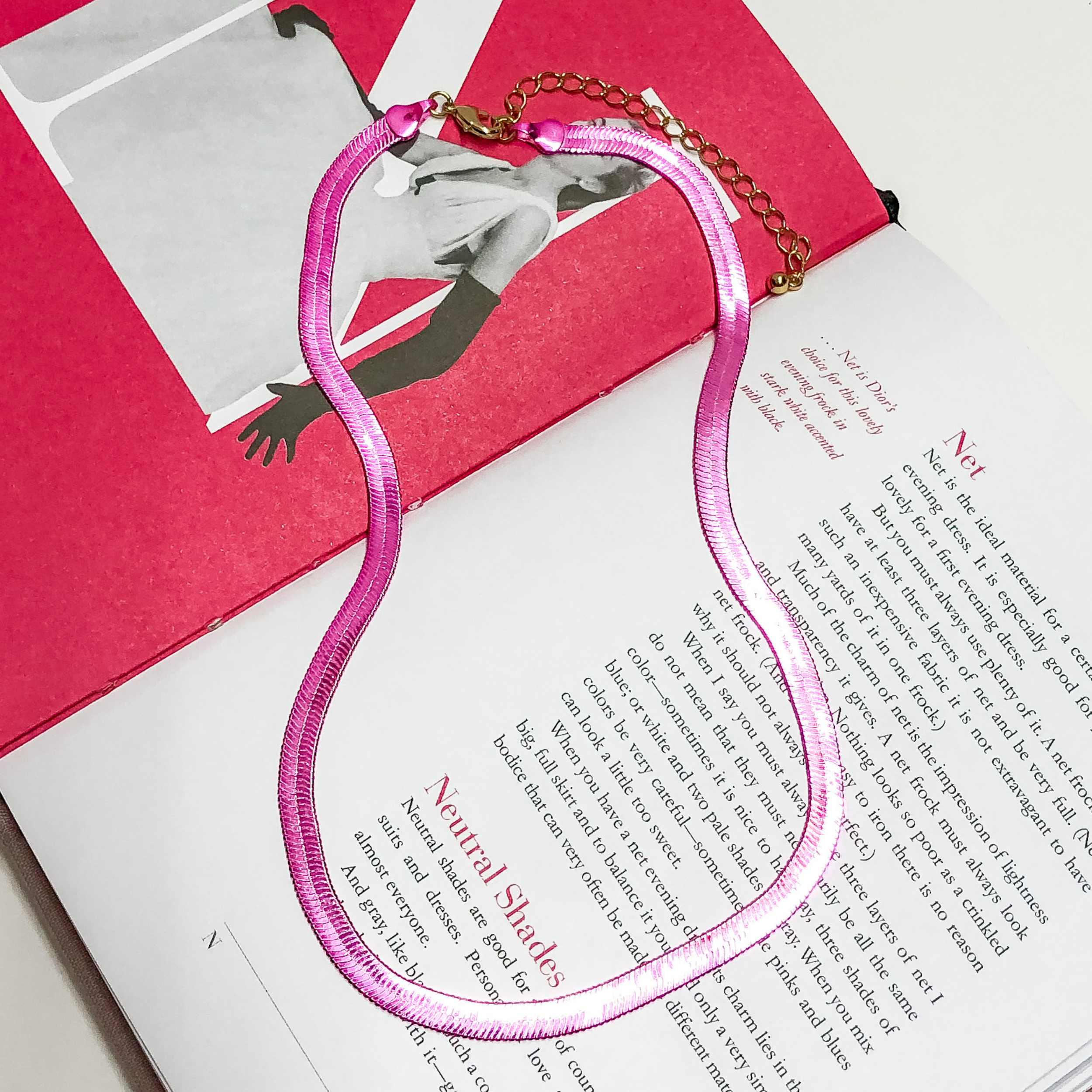 Pink Herringbone chain with a gold extender. This necklace is on a opened book, on a white background. 