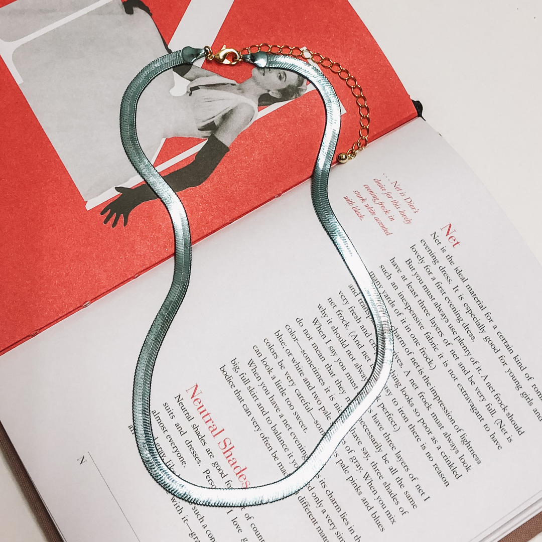 Grey Herringbone chain with a gold extender. This necklace is on a opened book, on a white background. 