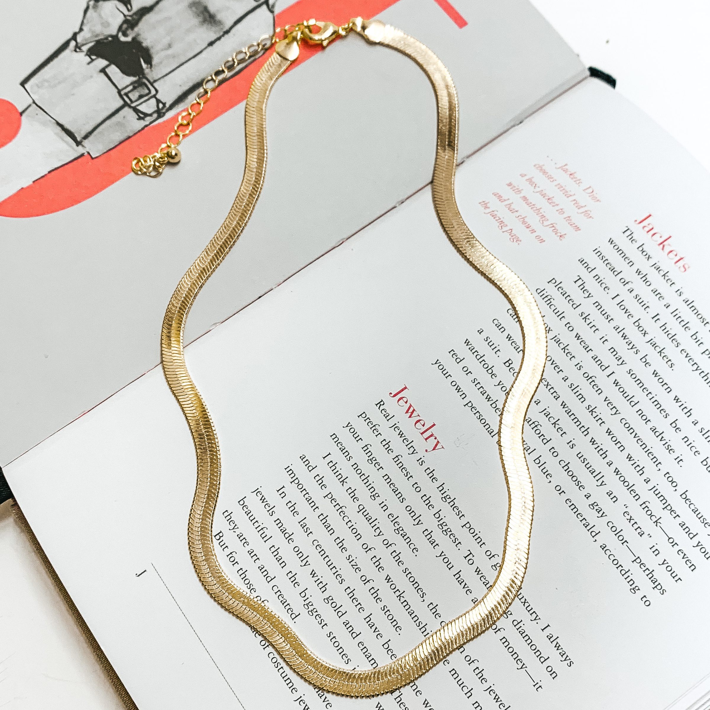 Gold herringbone chain necklace. This necklace is pictured on an open book on a white background. 