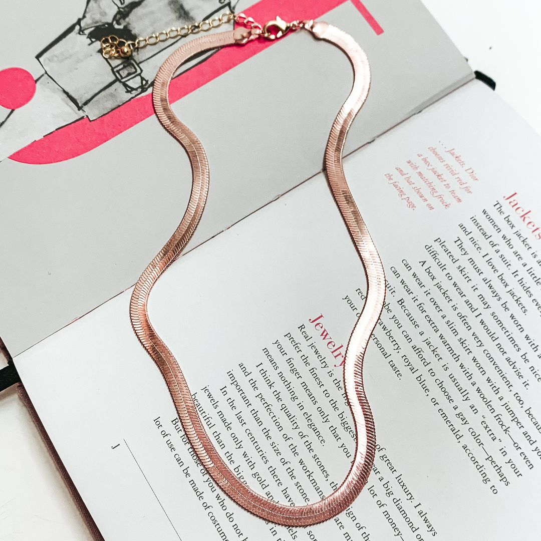 Light pink herringbone chain necklace. This necklace is pictured on an open book on a white background. 