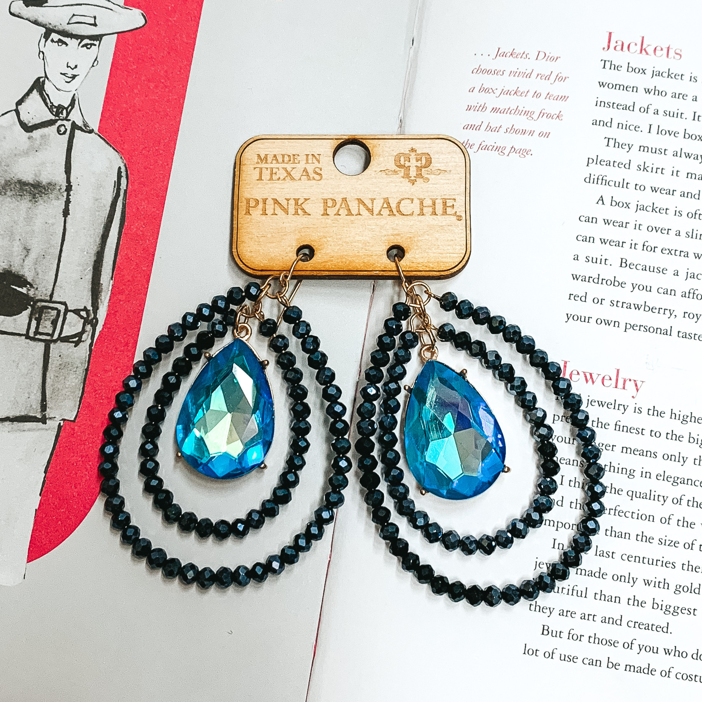 Double layered black crystal beaded teardop earrings with a center teardrop blue ab crystal. These earrings are pictured on an open book.