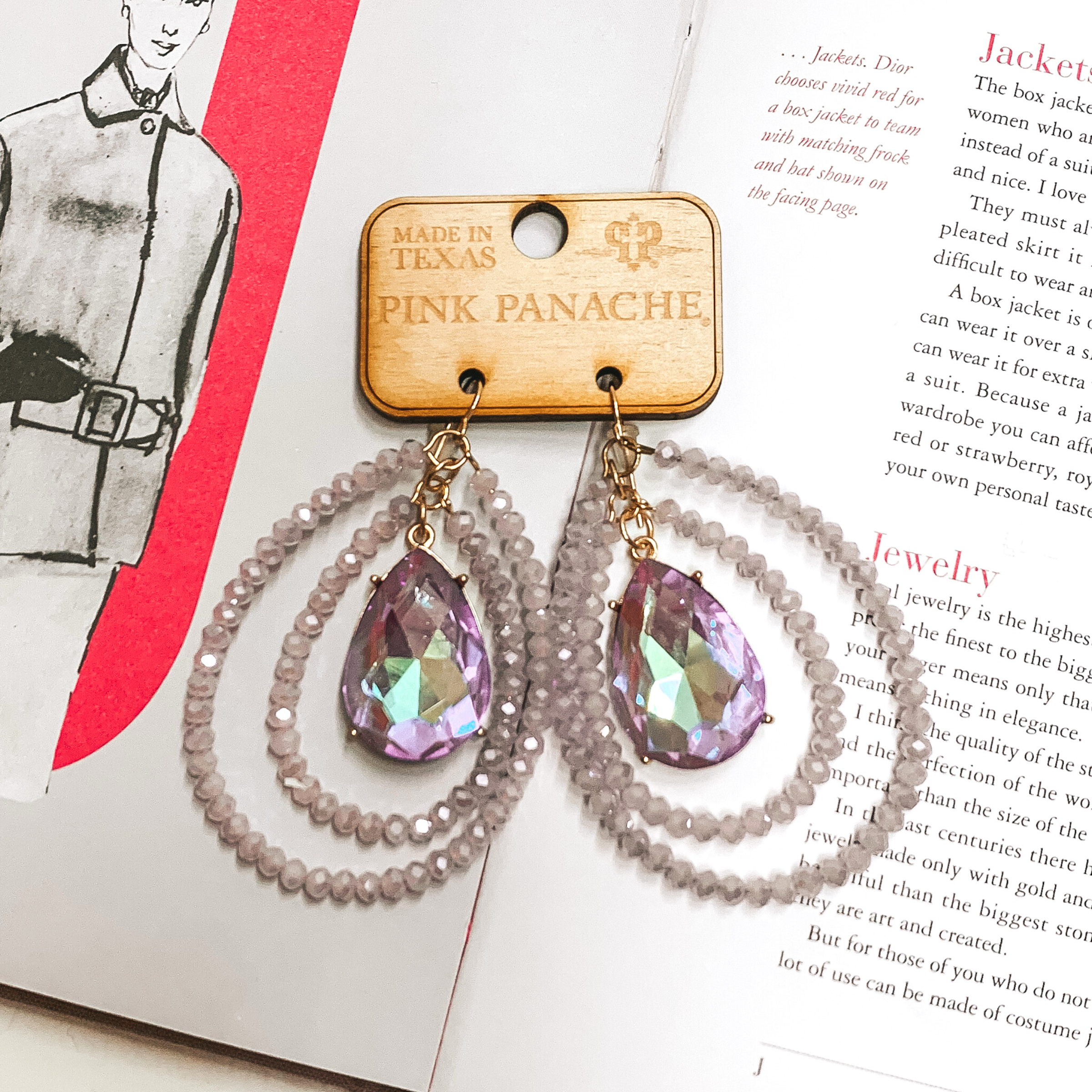 Double layered lavender crystal beaded teardop earrings with a center teardrop purple ab crystal. These earrings are pictured on an open book. 