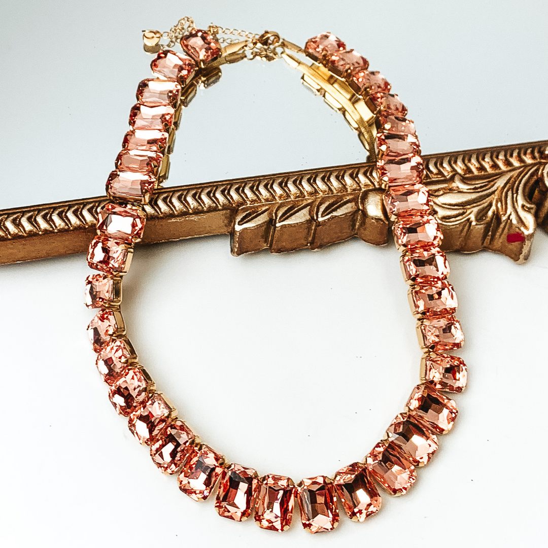 Rose gold, rectangle crystal necklace. This necklace is pictured partially laying on a gold mirror on a white background. 