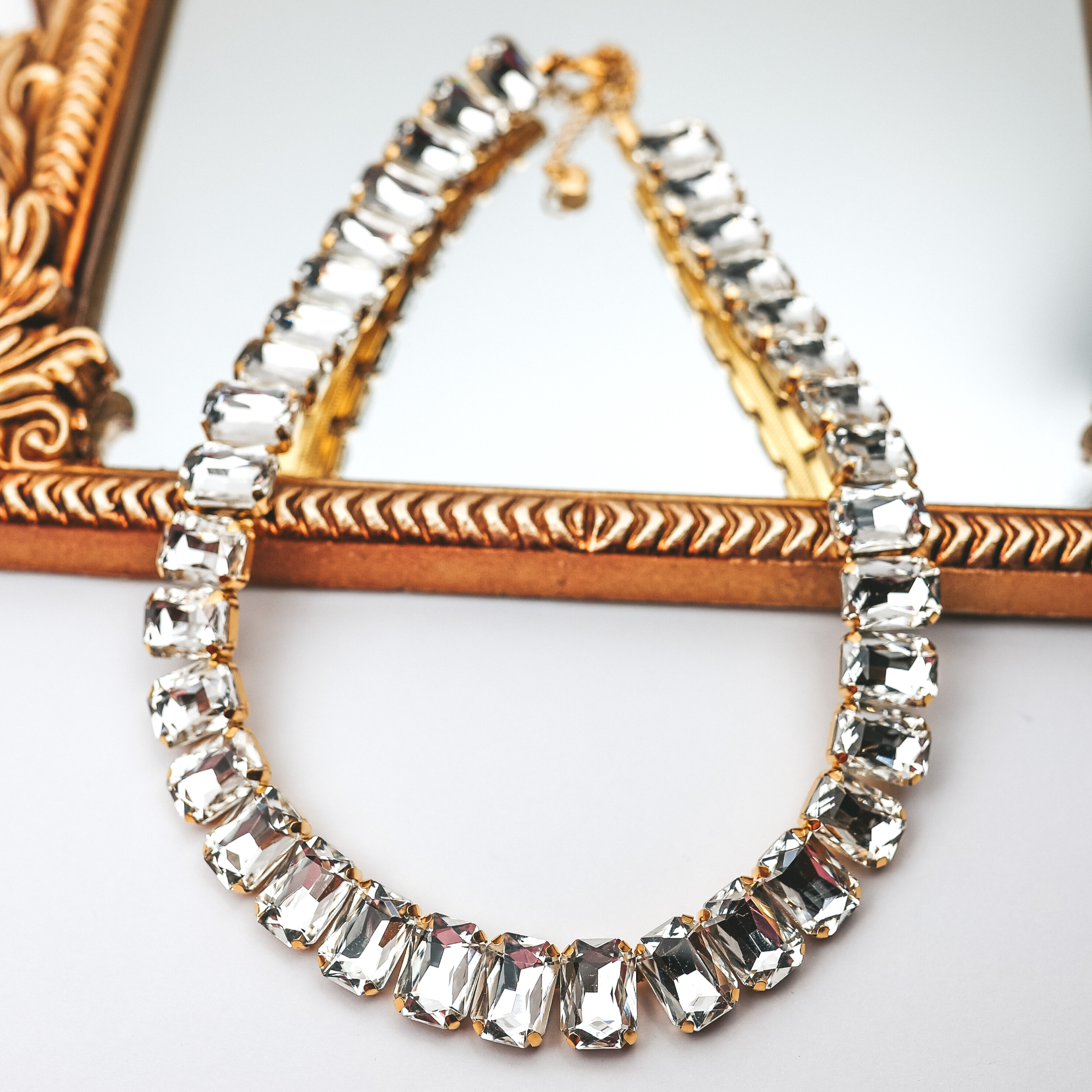 Clear, rectangle crystal bracelet. This necklace is pictured laying on a gold mirror on a white background. 