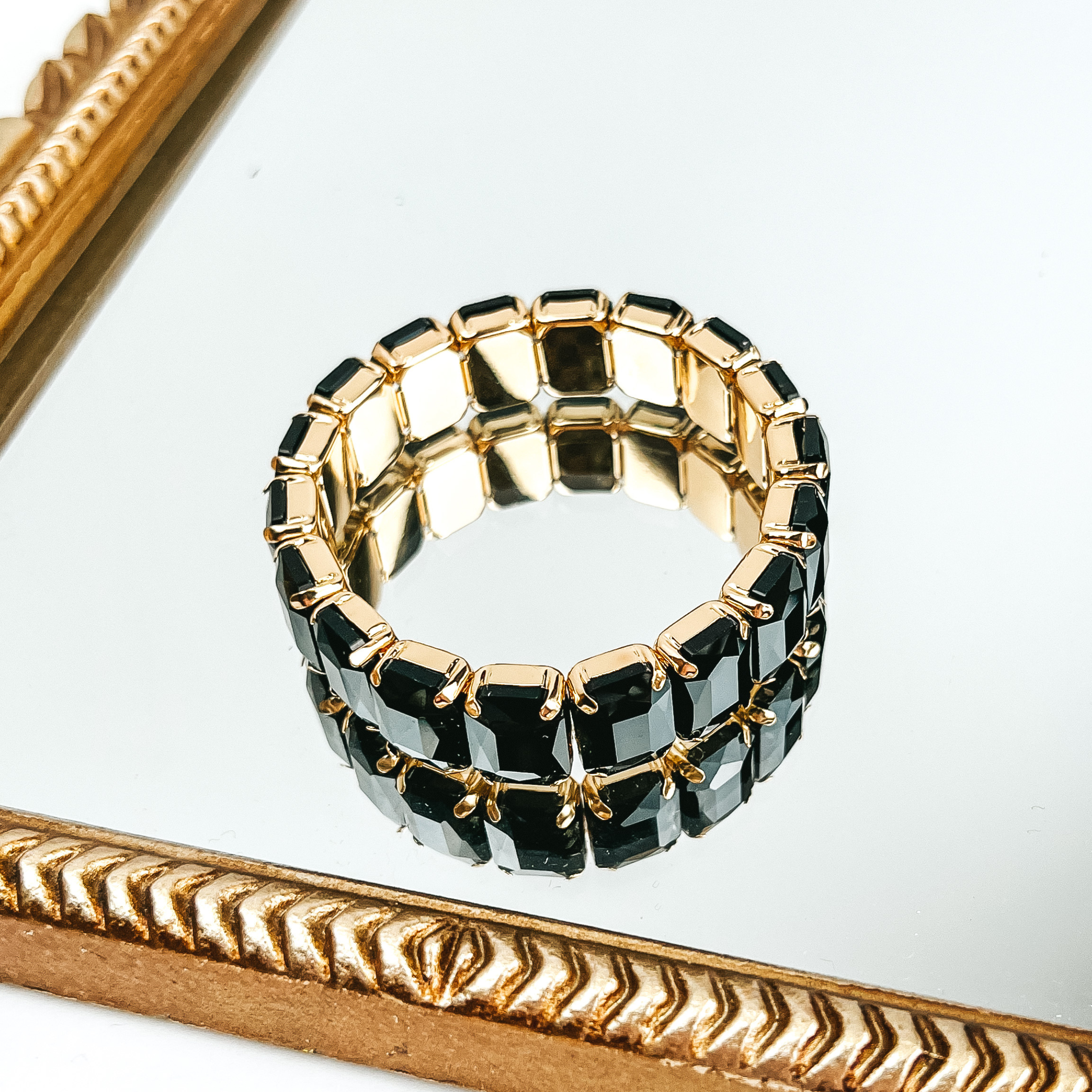 Black, rectangle crystal bracelet. This bracelet is pictured laying on a gold mirror on a white background. 