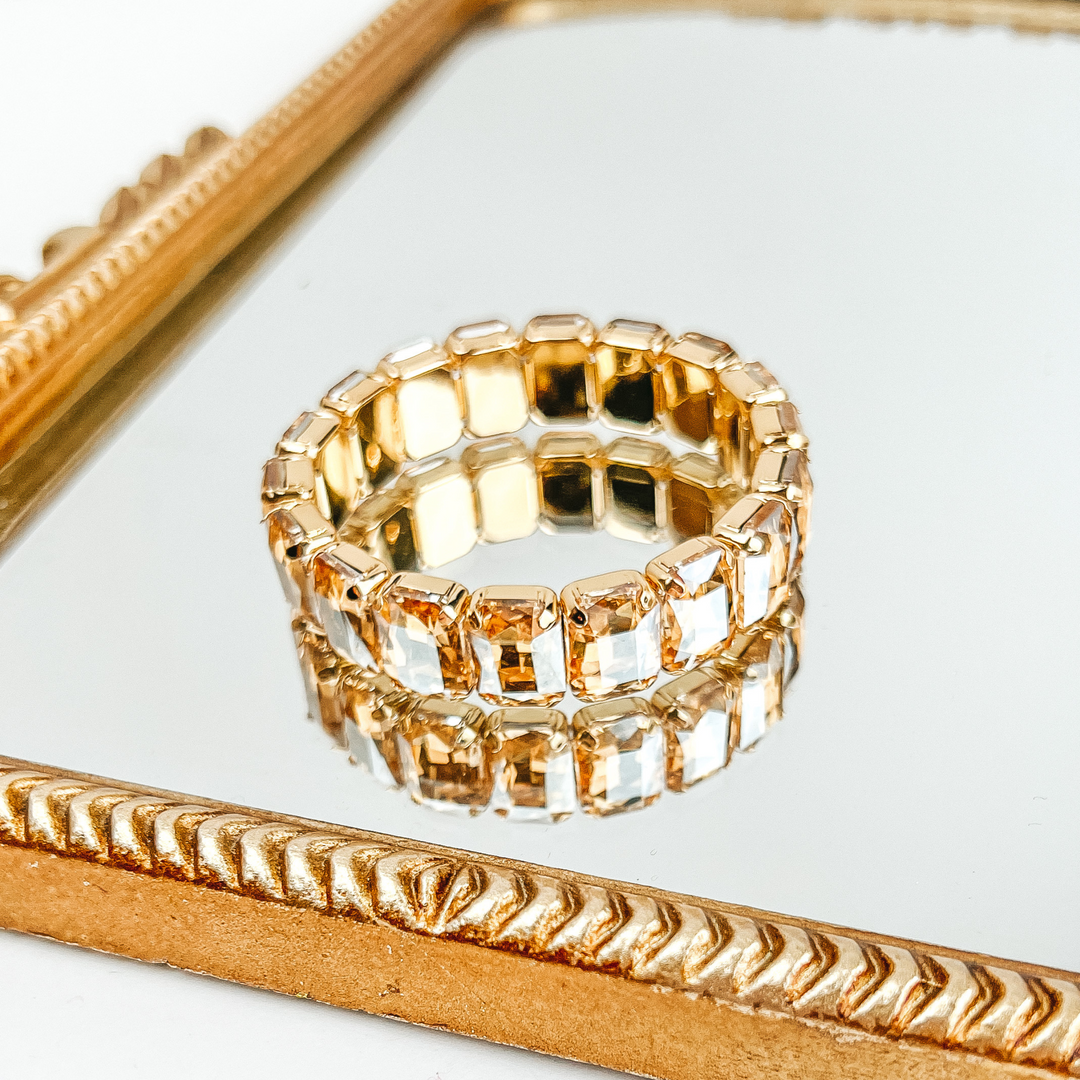 Beige, rectangle crystal bracelet. This necklace is pictured laying on a gold mirror on a white background. 