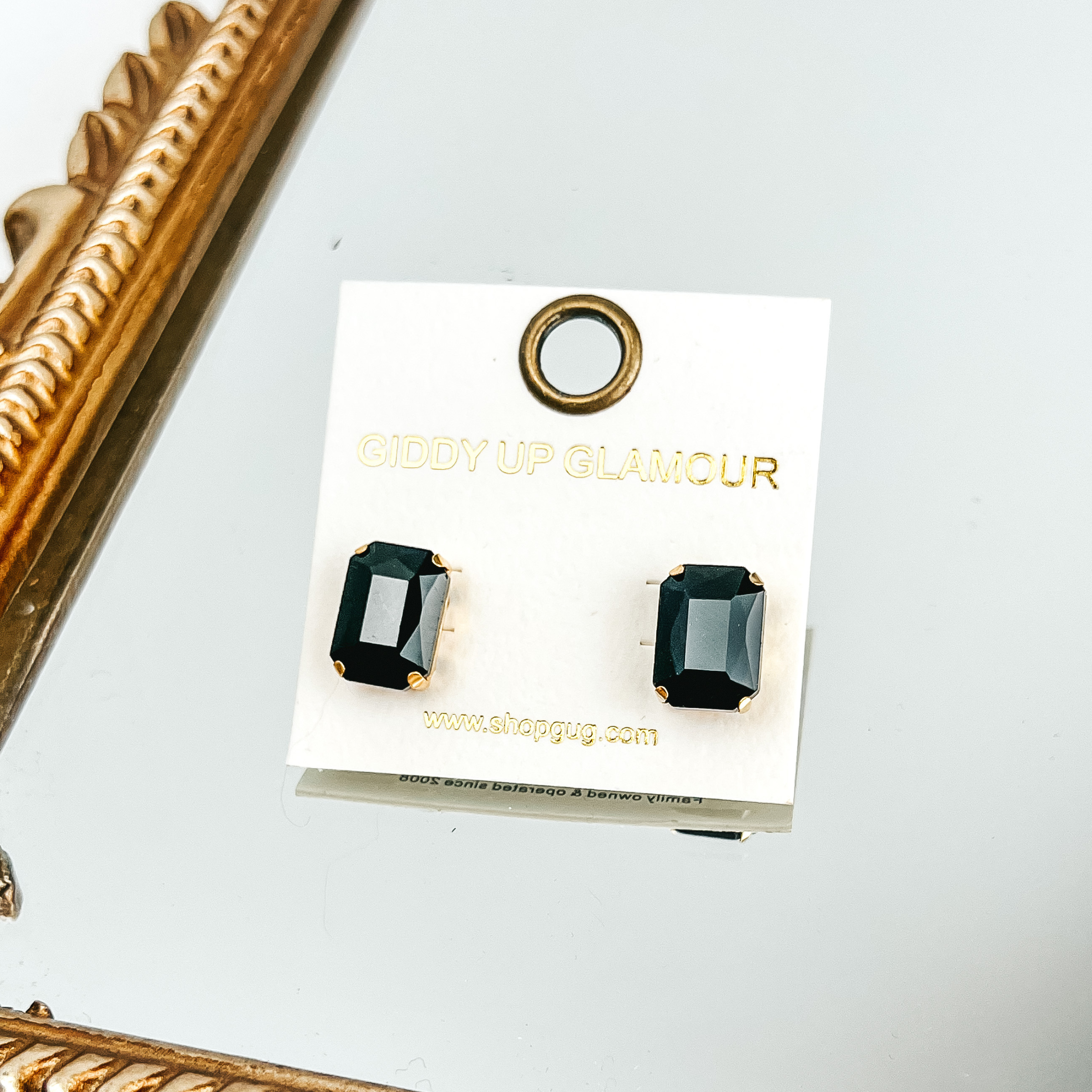 Black, rectangle crystal earrings on a white earrings holder. This bracelet is pictured laying on a gold mirror on a white background. 