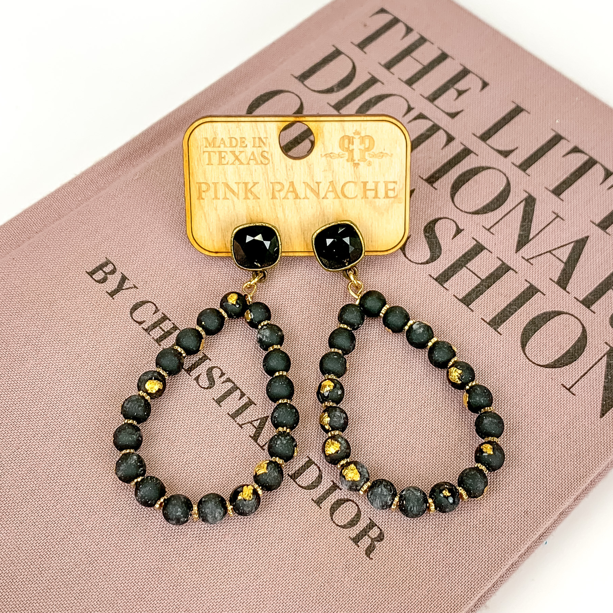 Black square stud earrings with a black beaded teardrop pendant. The pendant includes gold disk bead spacers and gold flakes on the beads. These earrings are pictured on a white background with a gold chain behind the earrings. 