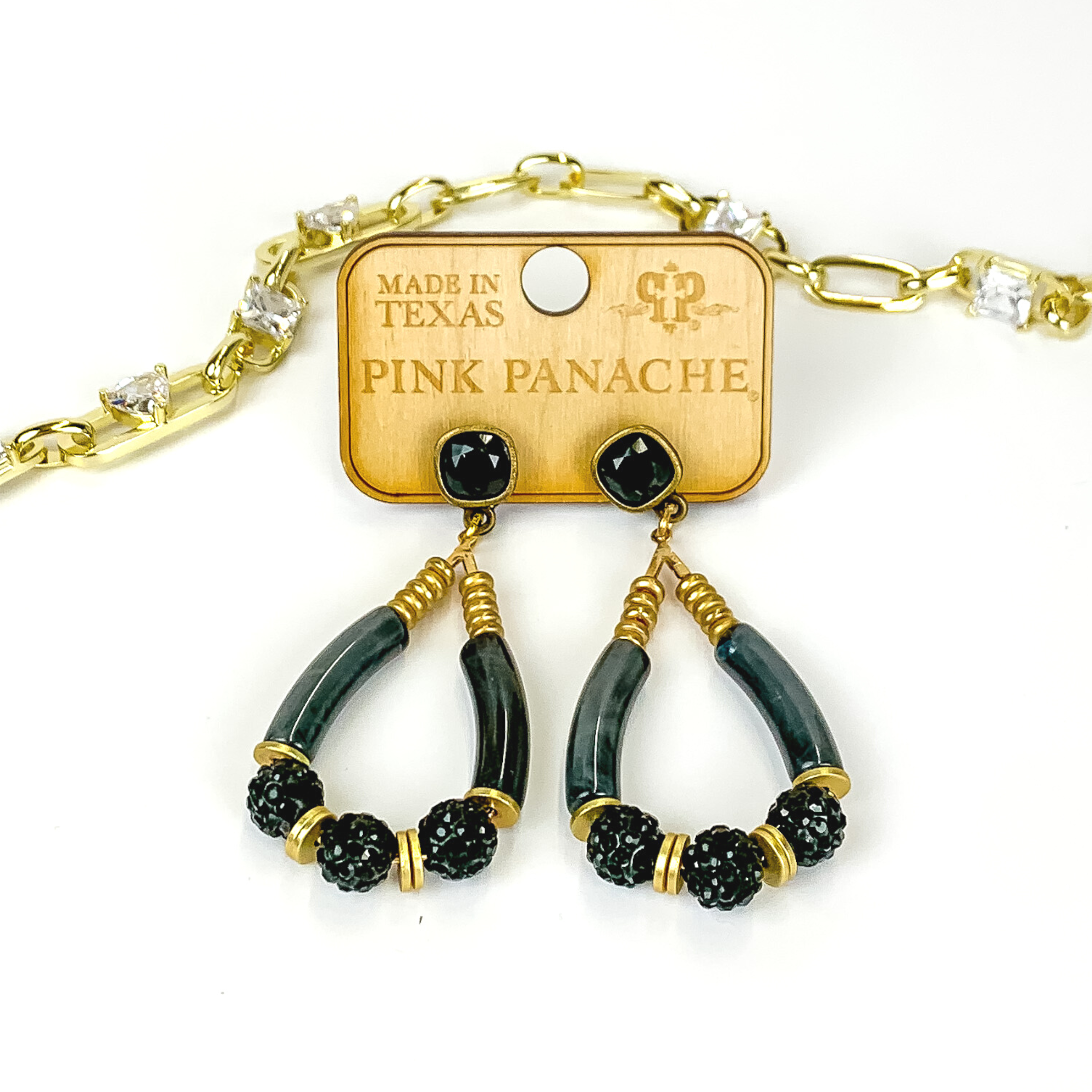 Black square stud earrings with a gold and black beaded teardrop pendant. The pendant includes gold disk beads, black marble tube beads, and black crystal beads. These earrings are pictured on a white background with a gold chain behind the earrings. 