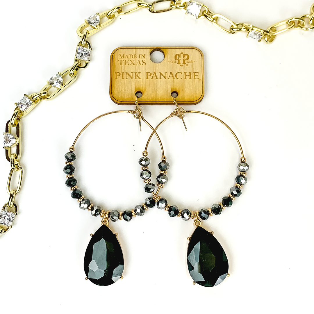 Gold hoop earrings with black crystal beads and gold spacer beads. These earrings also include a large black, teardrop crystal. These earrings are pictured on a top of a mauve colored book on a white background. 