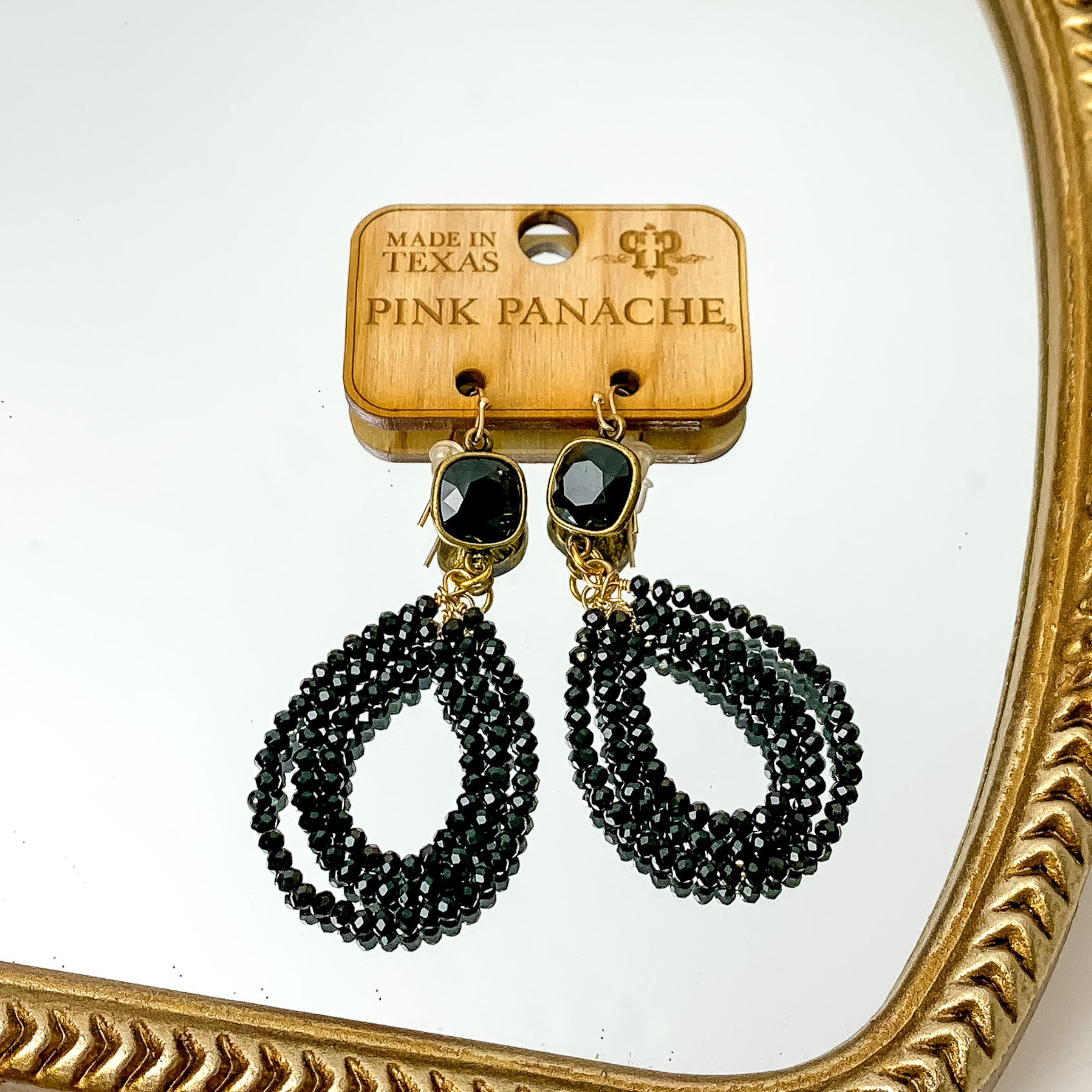 Black cushion cut crystal with a three layered, black beaded teardrop pendant. These earrings are pictured on a gold mirror. 