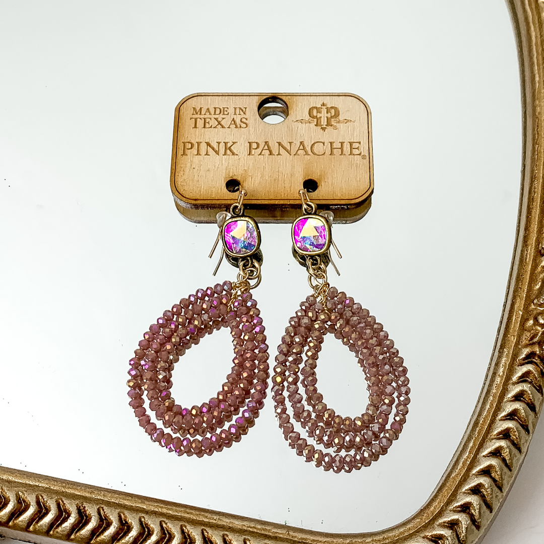 Ab cushion cut crystal with a three layered, ab purple beaded teardrop pendant. These earrings are pictured on a gold mirror. 