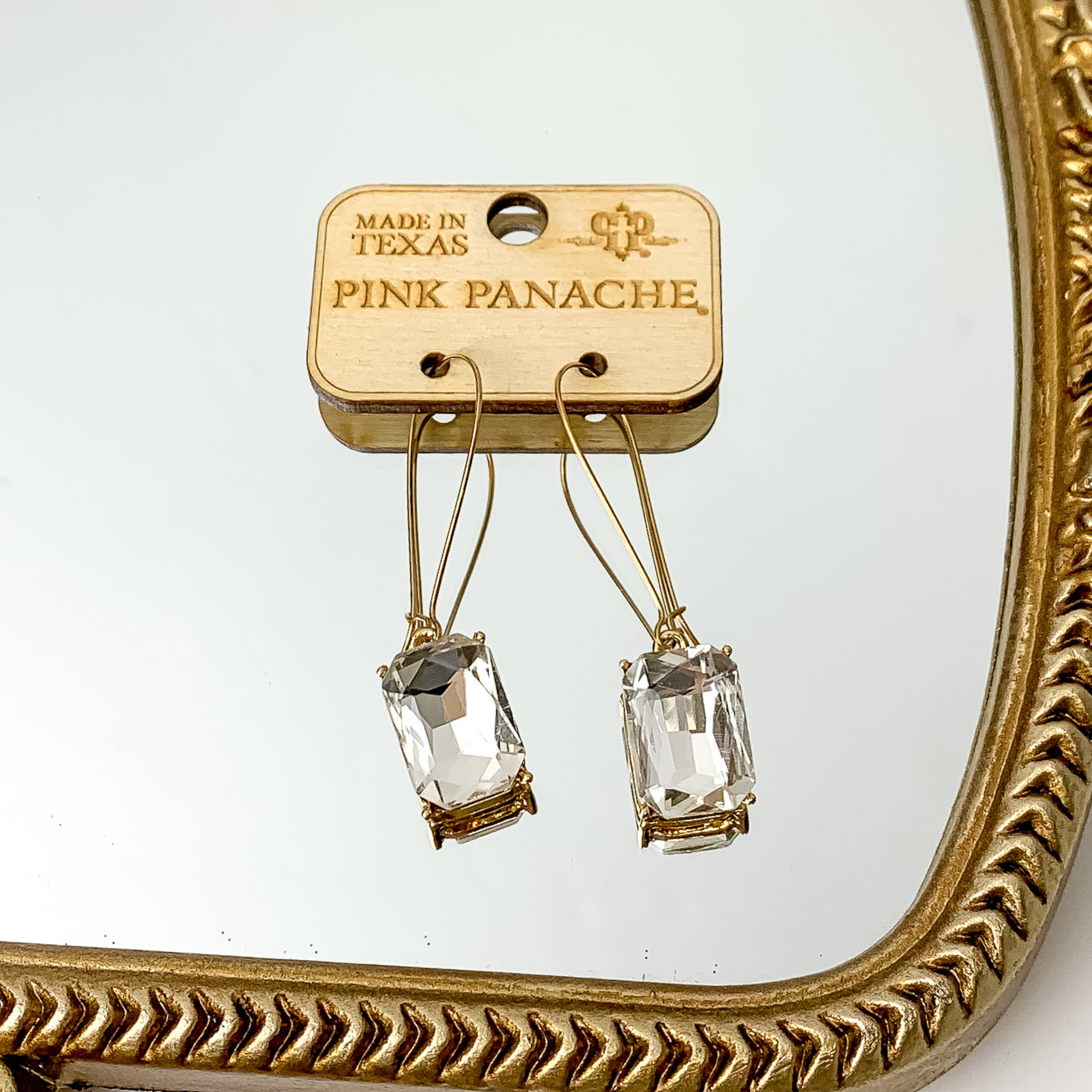 Gold kidney wire earrings with a rectangle, clear crystal charm. These earrings are pictured on a mirror.