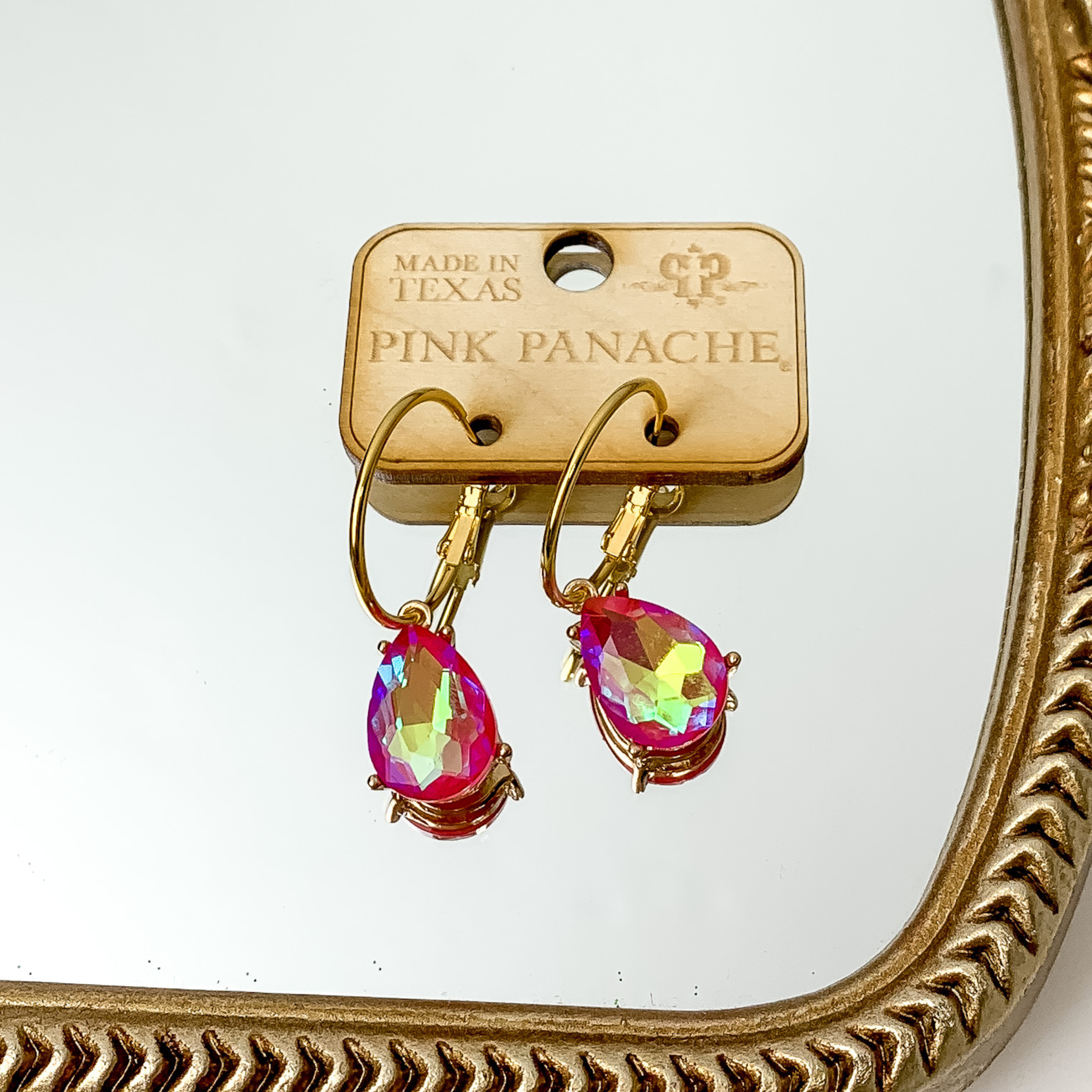 Gold hoop earrings with a fuchsia teardrop crystal charm. These earrings are pictured on a gold mirror. 