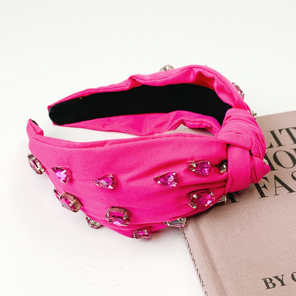 Fuchsia colored knot headband with different shaped fuchsia crystals. This headband is pictured partially laying on a mauve book on a white background. 