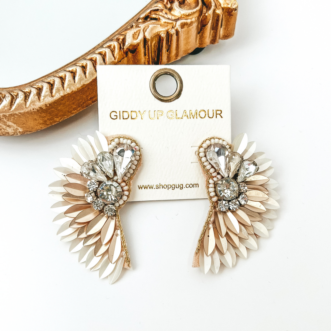White and light gold, sequin feather earrings with a clear crystal design. These earrings are pictured on a white background with a gold mirror in the top left corner. 