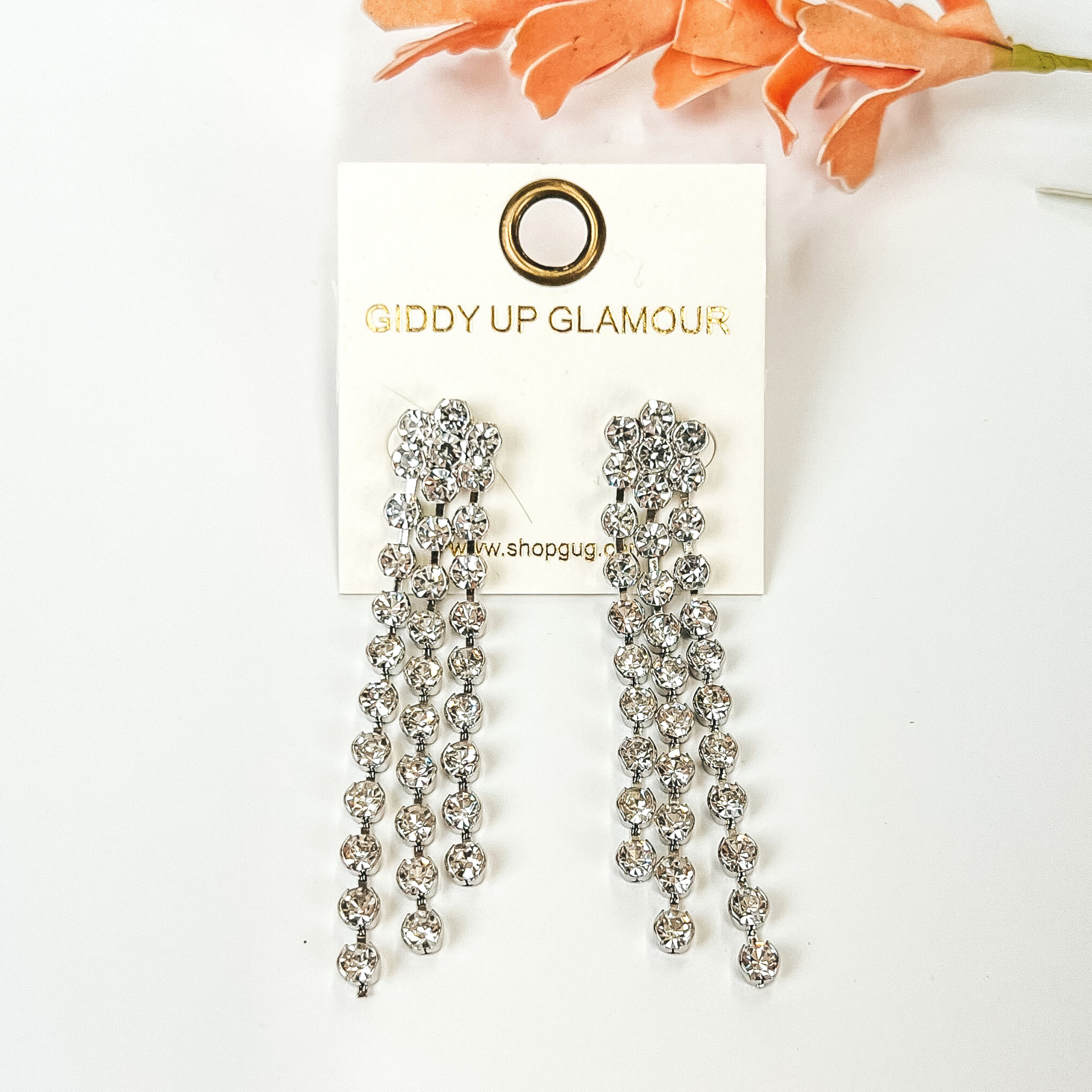 Clear crystal tassel earrings with a silver backing. These earrings are pictured on a white background with an orange flower above the earrings.