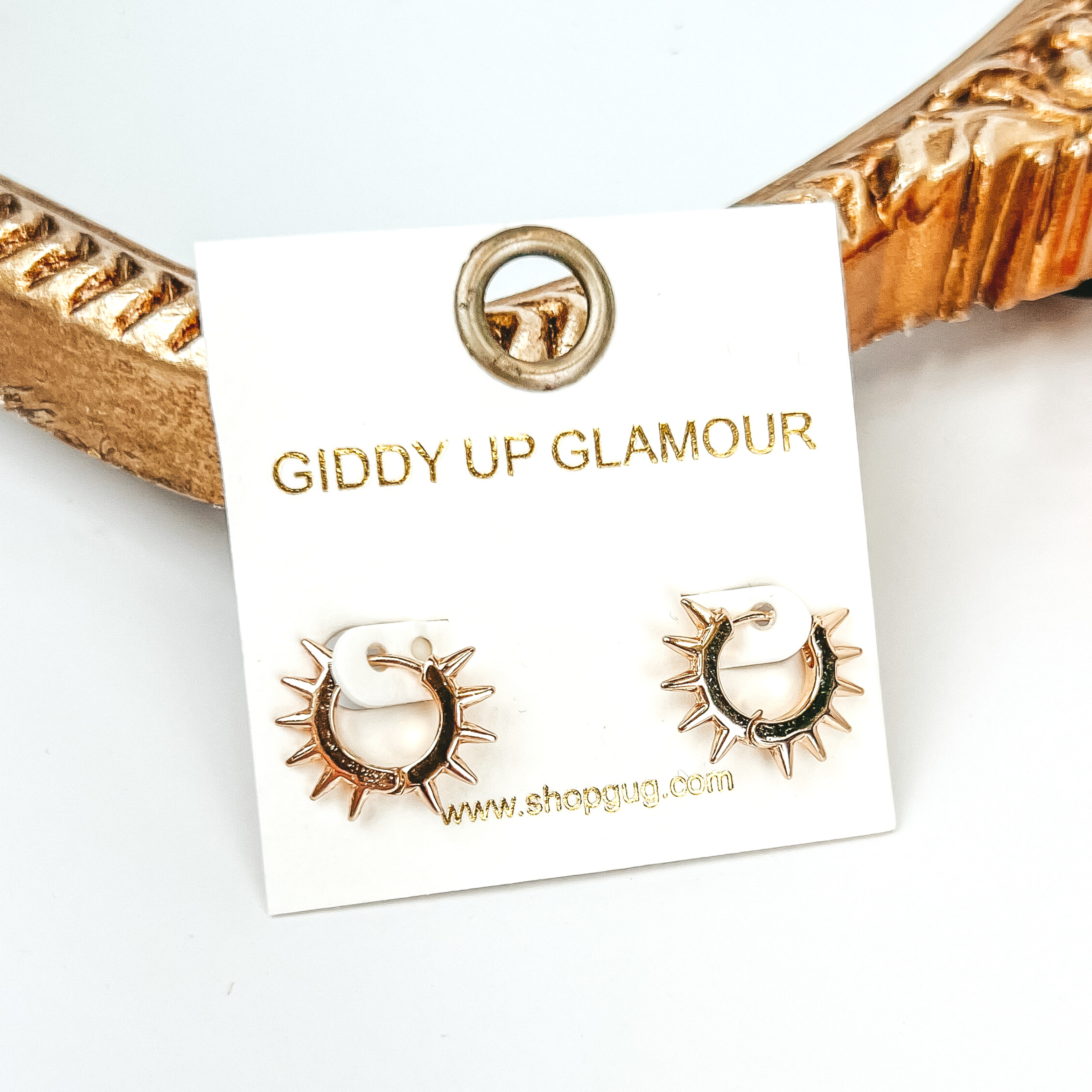 Starburst gold hoop earrings pictured on a white background in front of a gold mirror.