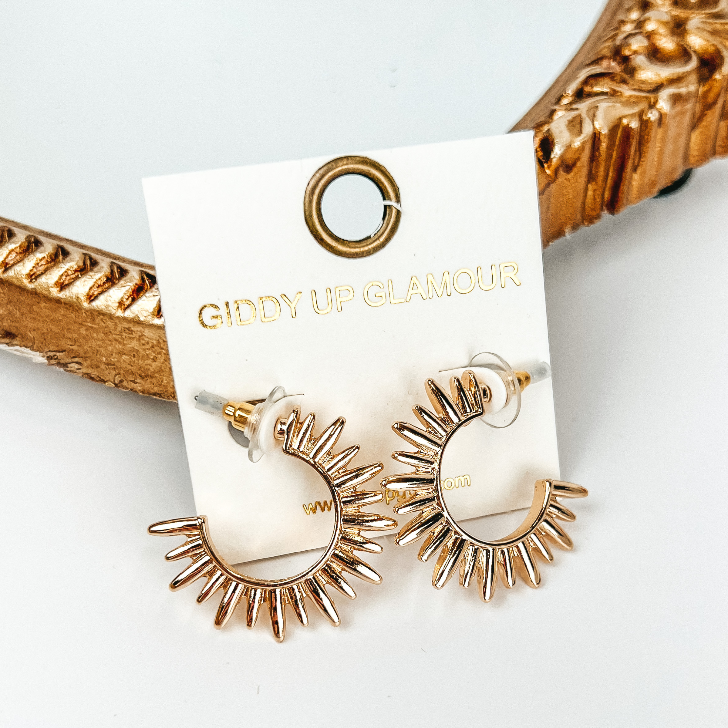 Gold sunburst hoop earrings. These earrings are pictured on a white background with a gold mirror behind the earrings. 