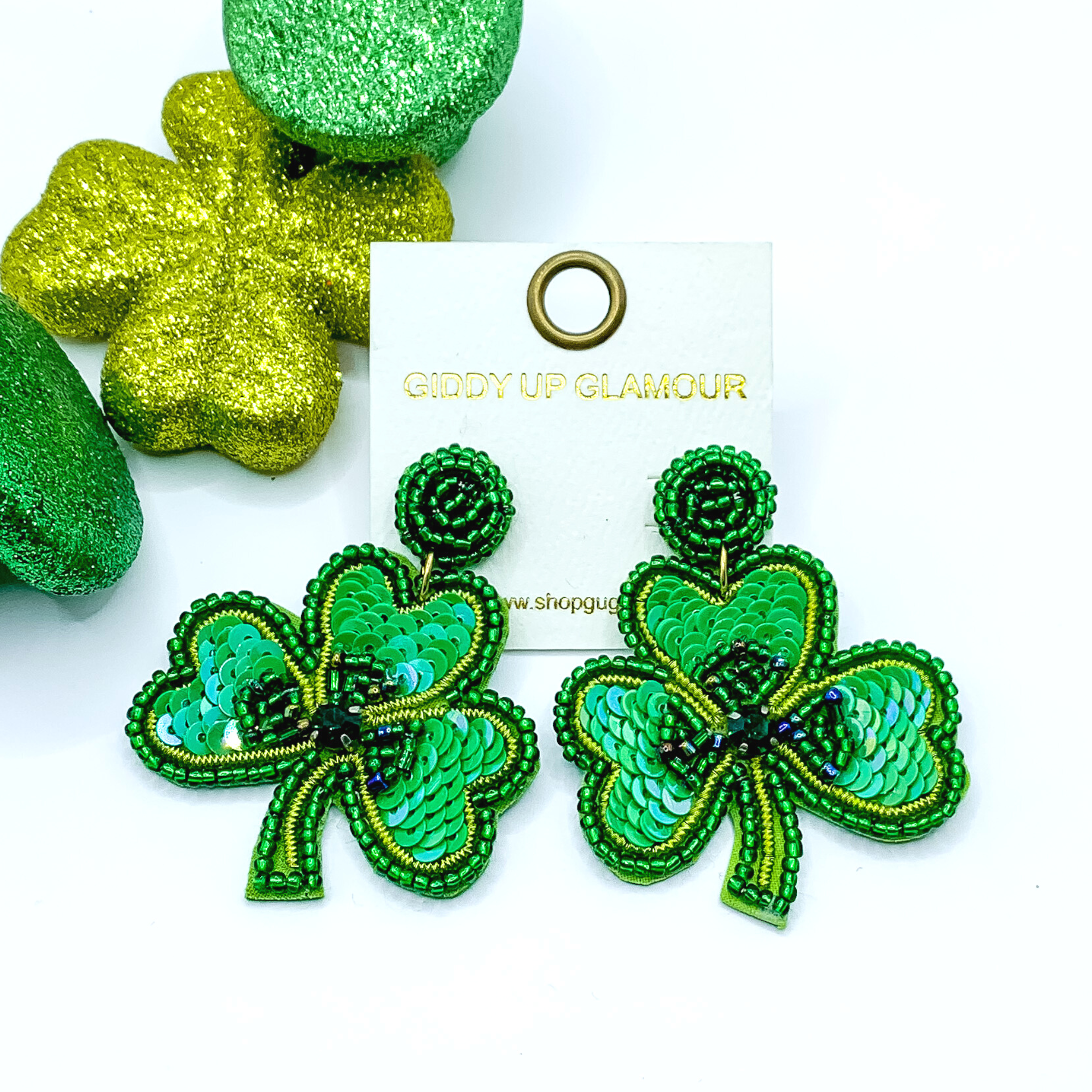 Green beaded shamrock earrings with green sequins. These earrings are pictured on a white background with green decor in the top left corner. 