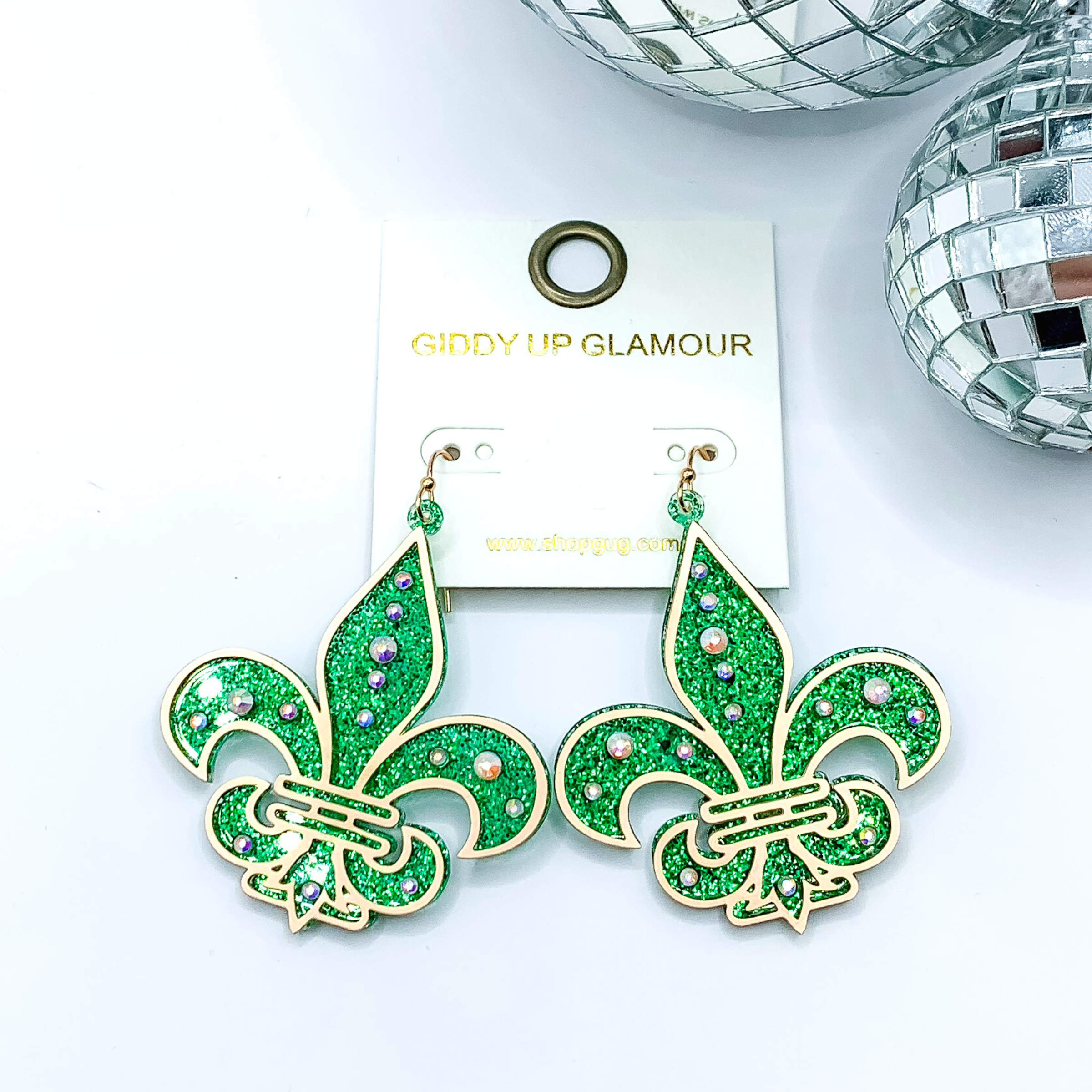 Green glitter fleur de lis dangle earrings. These earrings include a gold outline and ab crystals. These earrings are pictured on a white background with disco balls in the top right corner.
