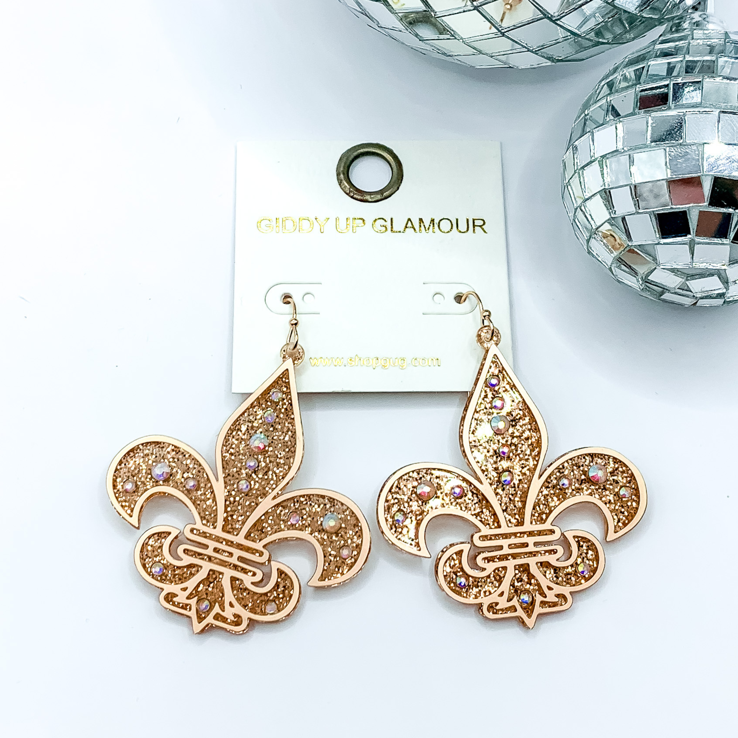 Gold glitter fleur de lis dangle earrings. These earrings include a gold outline and ab crystals. These earrings are pictured on a white background with disco balls in the top right corner.