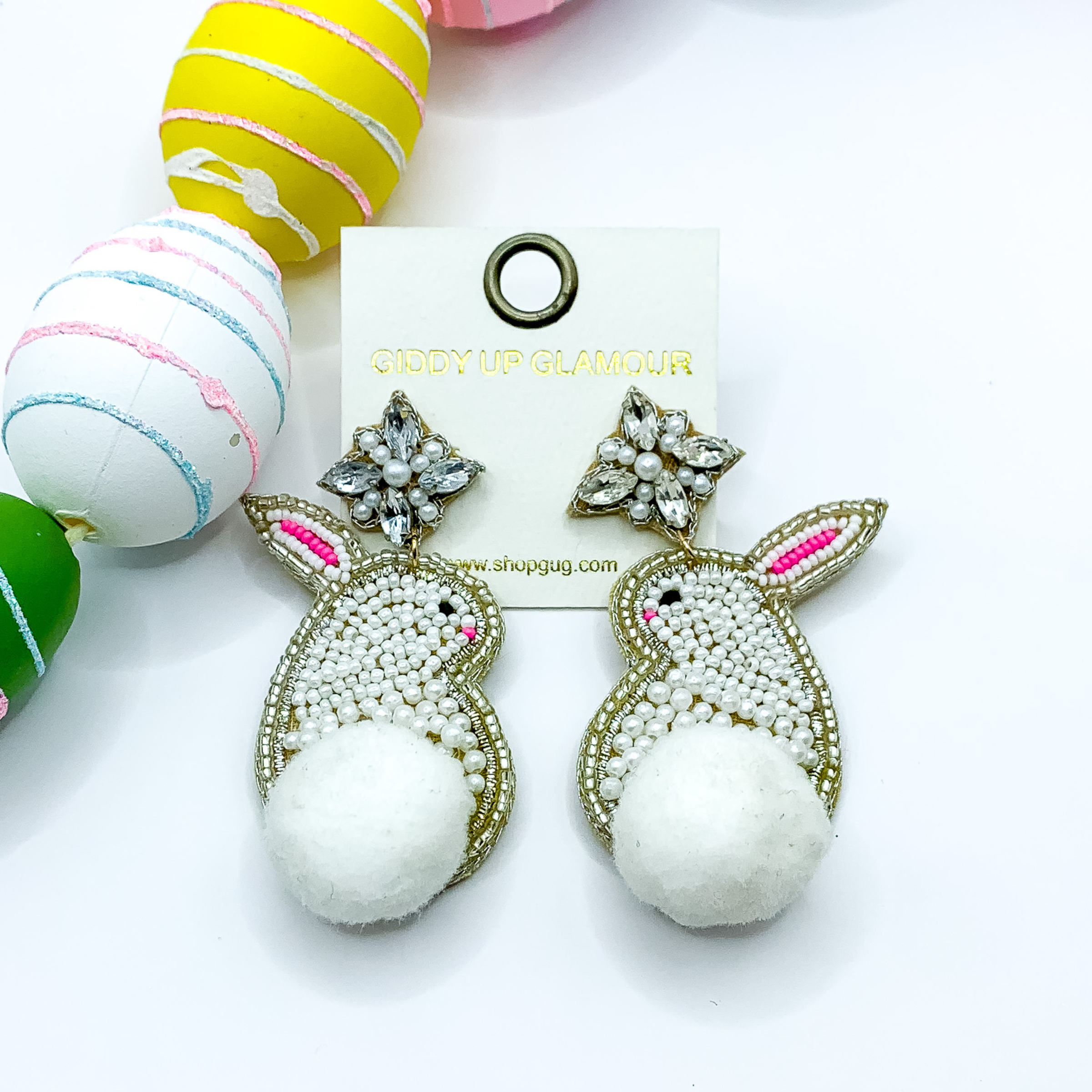 Beaded, white bunny rabbit earrings on a crystal post with a white puff ball for a tail. Pictured on white background with colorful Easter eggs.