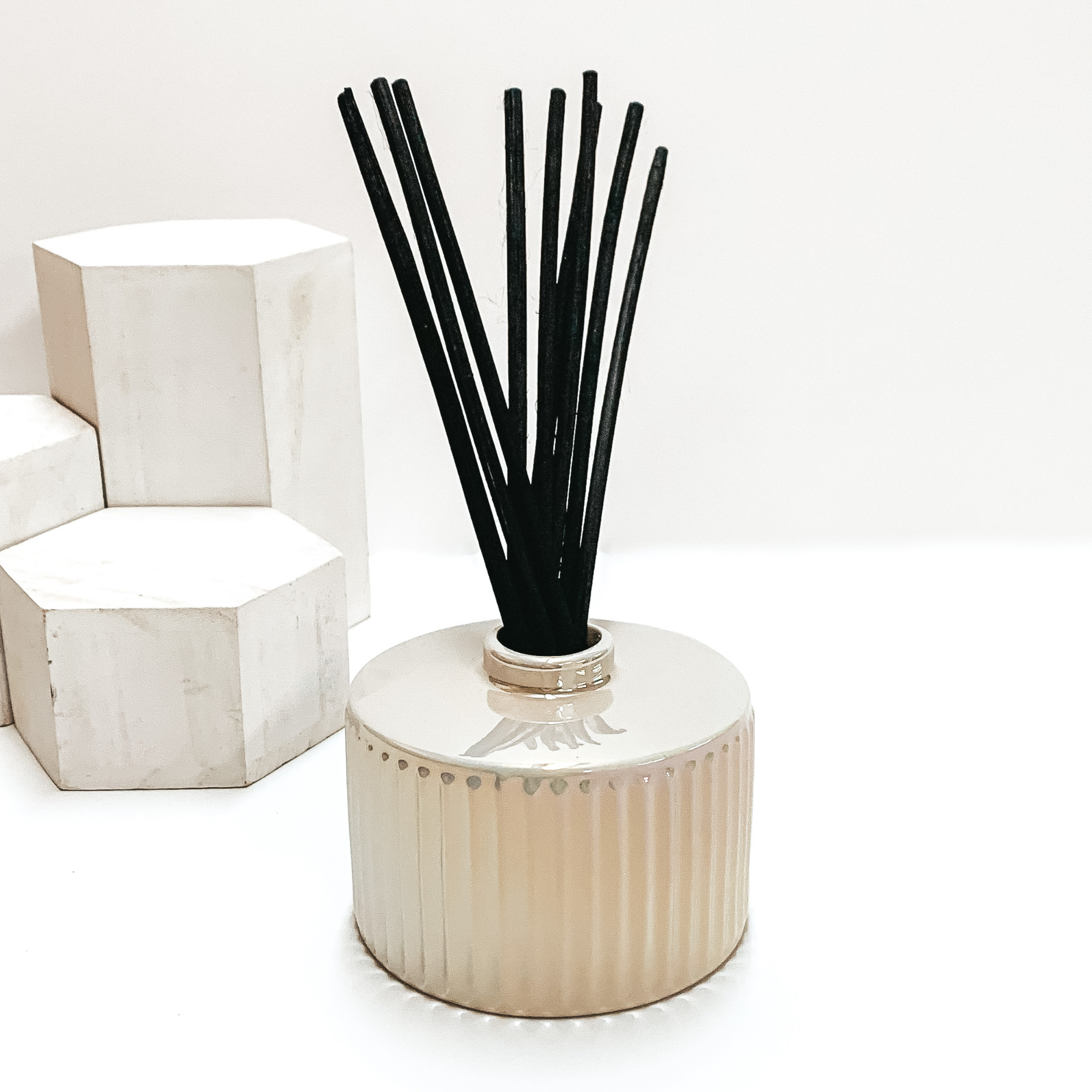 White opal diffuser holder with black reeds sticking out of the top. This diffuser is pictured on a white background with white blocks on the left side of the candle. 