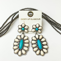 Silver, oval drop earrings with white stones and turquoise center stones. These earrings are pictured on a white background with silver beads behind the earrings. 