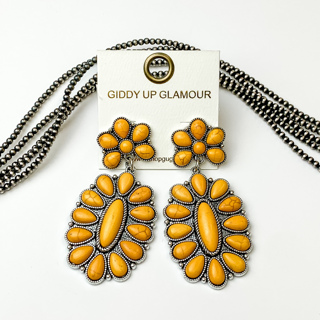 Silver, oval drop earrings with yellow stones. These earrings are pictured on a white background with silver beads behind the earrings. 