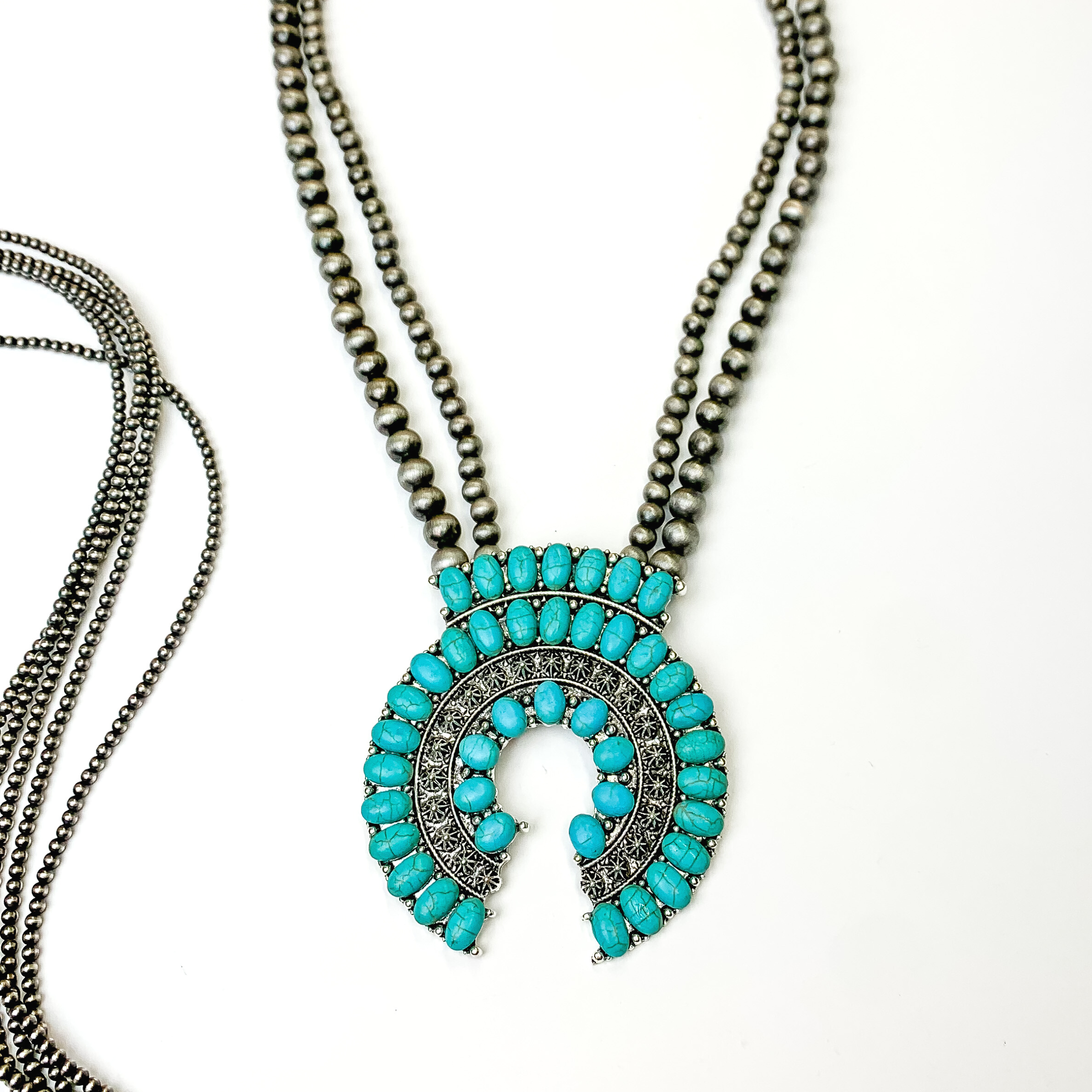 This silver beaded double strand necklace with silver naja pendant and turquoise stones covering it. This necklace is pictured on a white background with silver beads on the left side of the picture.   