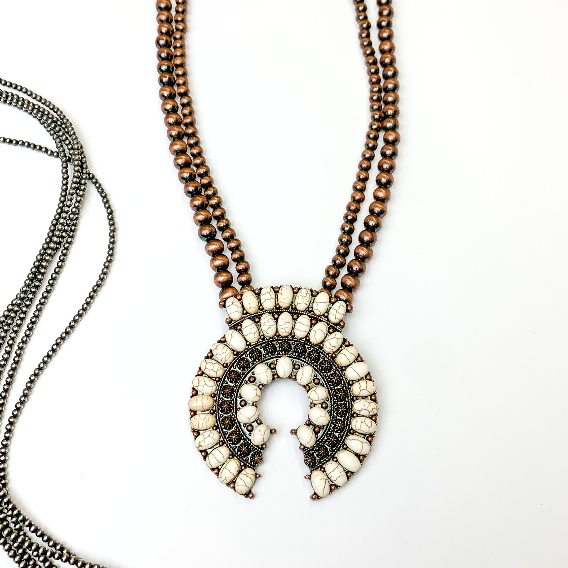 This copper beaded double strand necklace with copper naja pendant and ivory stones covering it. This necklace is pictured on a white background with silver beads on the left side of the picture.   