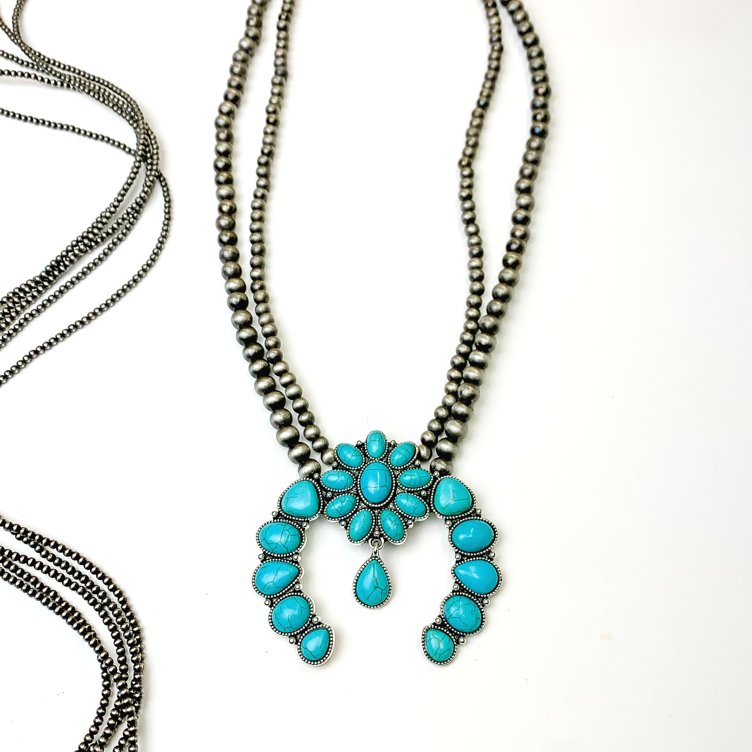 Double stran silver beaded necklace with a turquoise stone naja pendant. This necklace is pictured on a white background with silver beads on the left side of the picture.