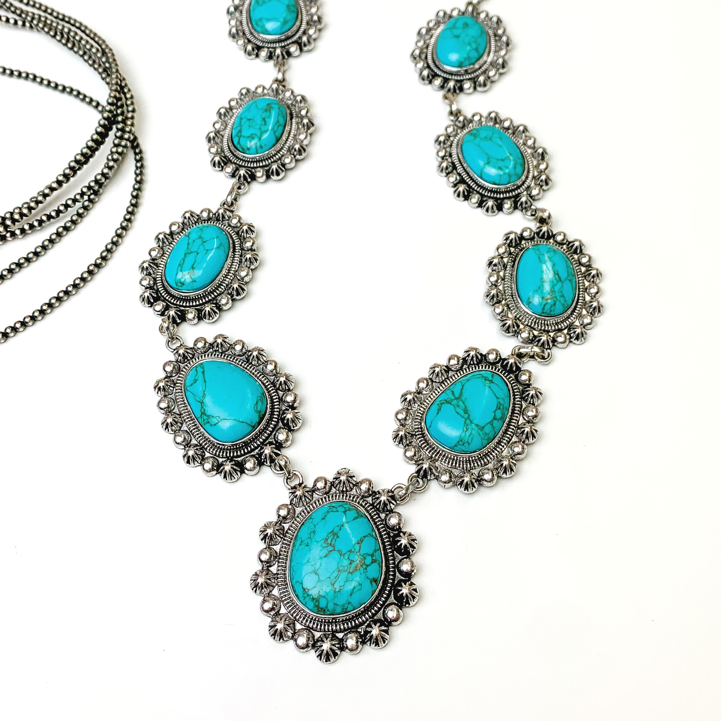 Silver necklace with circular turquoise stones. Each stone has a silver beaded outline. This necklace is pictured on a white background with silver beads on the left side of the picture.