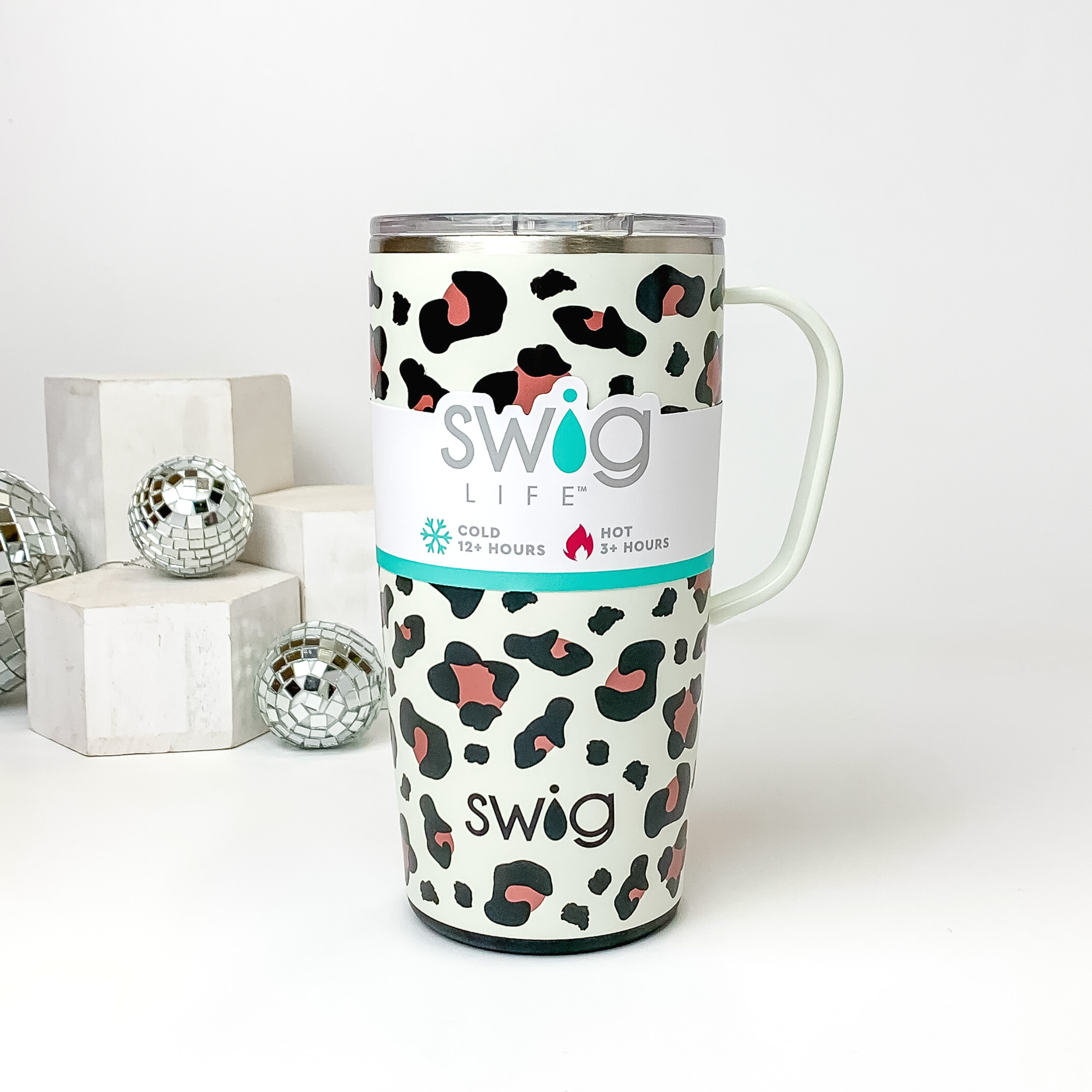 Ivory mug with a clear lid and ivory handle. This mug has a black and rose gold leopard print. this mug is pictured on a white background with white blocks and disco balls on the left side of the picture. 