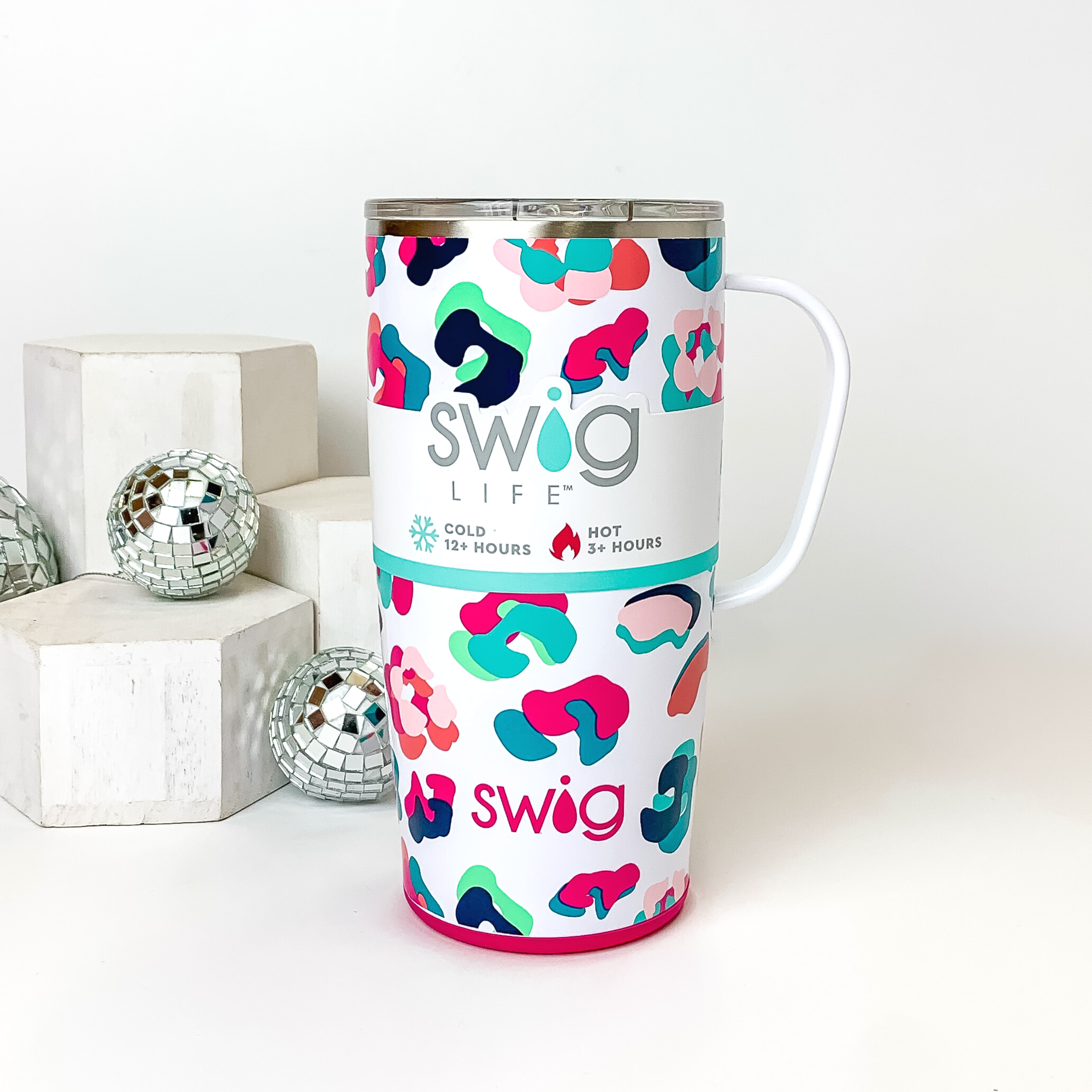 White mug with a clear lid and white handle. This mug has neon multicolored leopard print. This mug is pictured on a white background with white blocks and disco balls on the left side of the picture. 