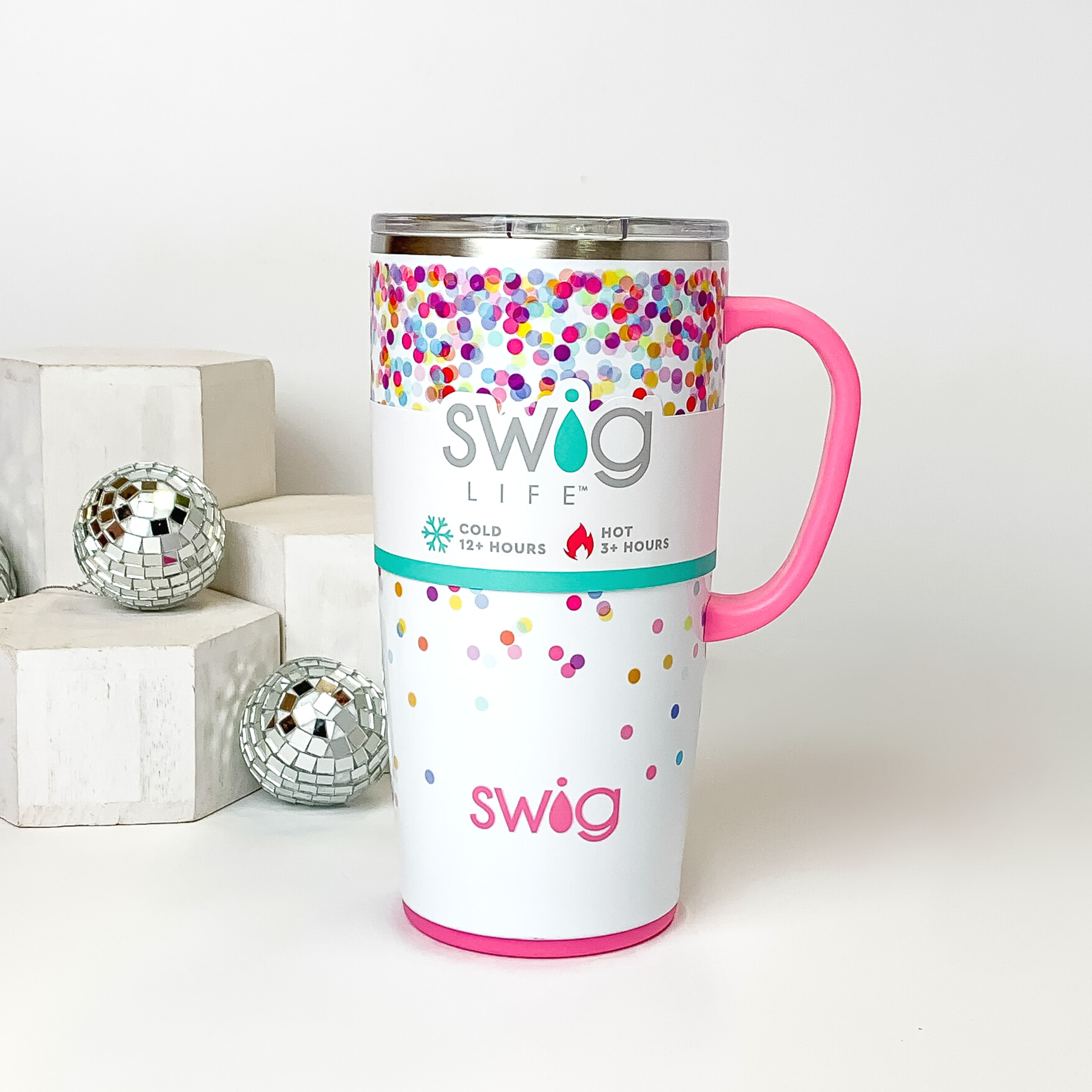 White mug with a clear lid and white handle. This mug has a multicolored confetti print. This mug is pictured on a white background with white blocks and disco balls on the left side of the picture. 