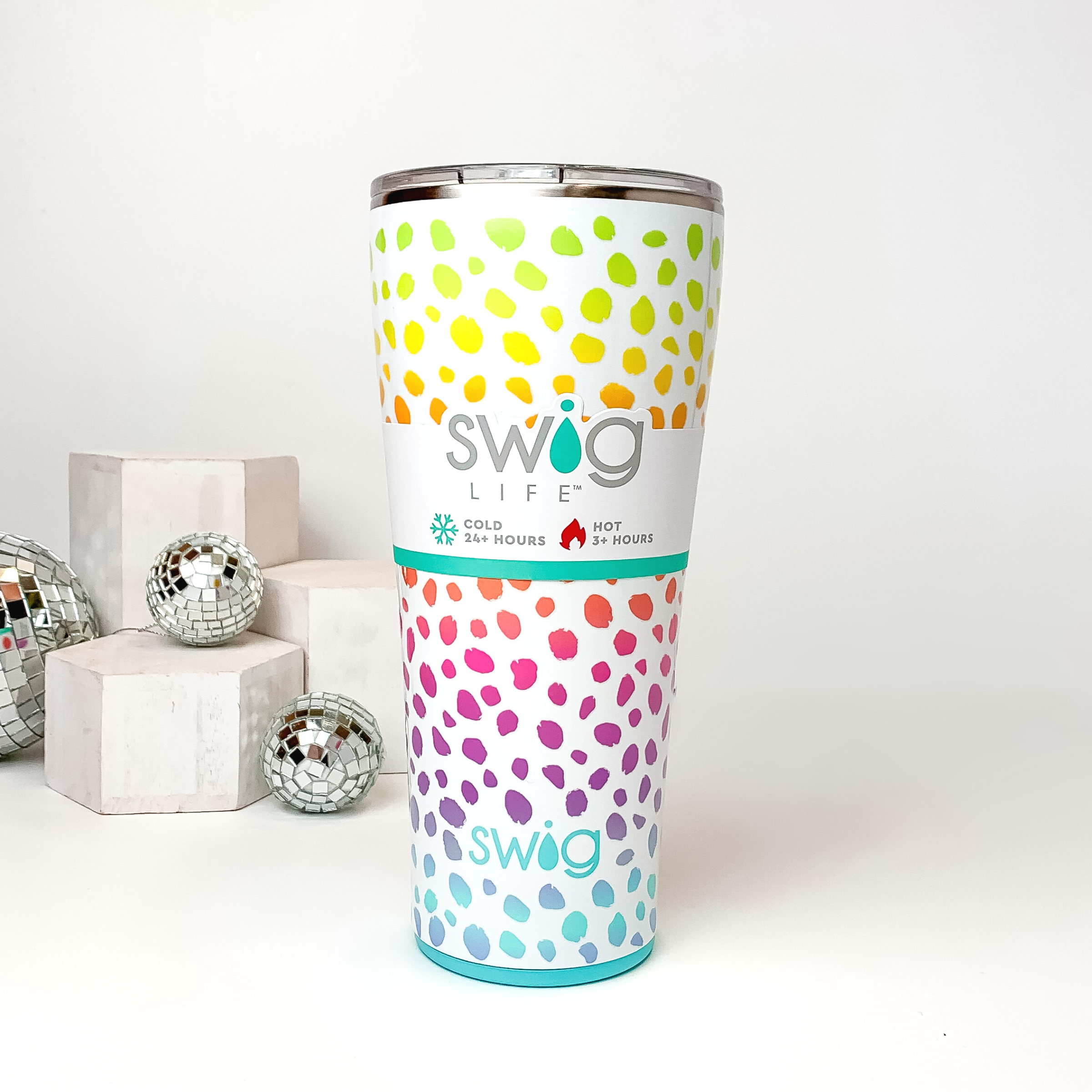 White tumbler with a clear lid. This tumbler includes a multicolored dotted print that is ombre. This tumbler is pictured on a white background with white blocks and disco balls on the left side of the picture. 