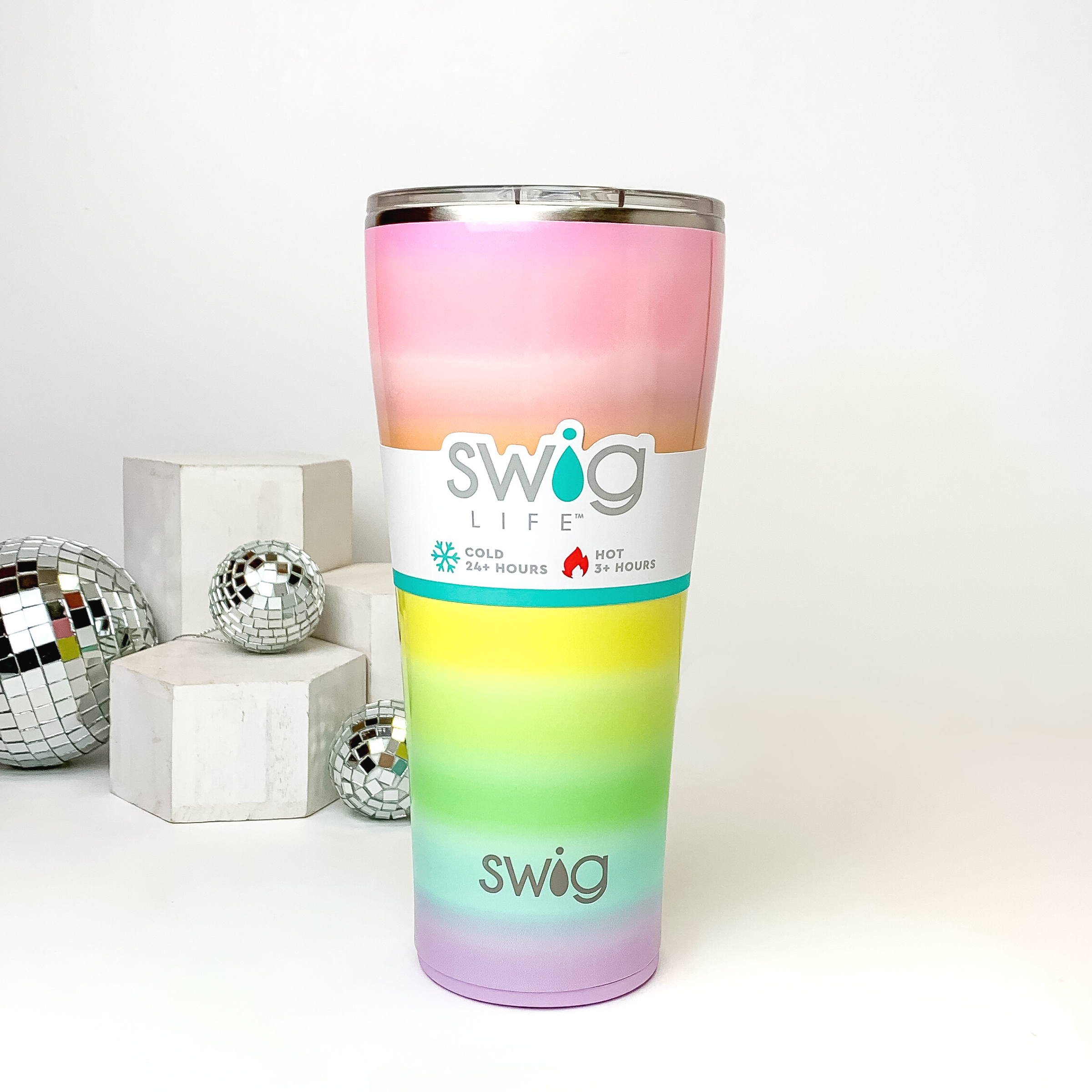 Ombre rainbow tumbler with a clear lid. This tumbler is pictured on a white background with white blocks and disco balls on the left side of the picture. 