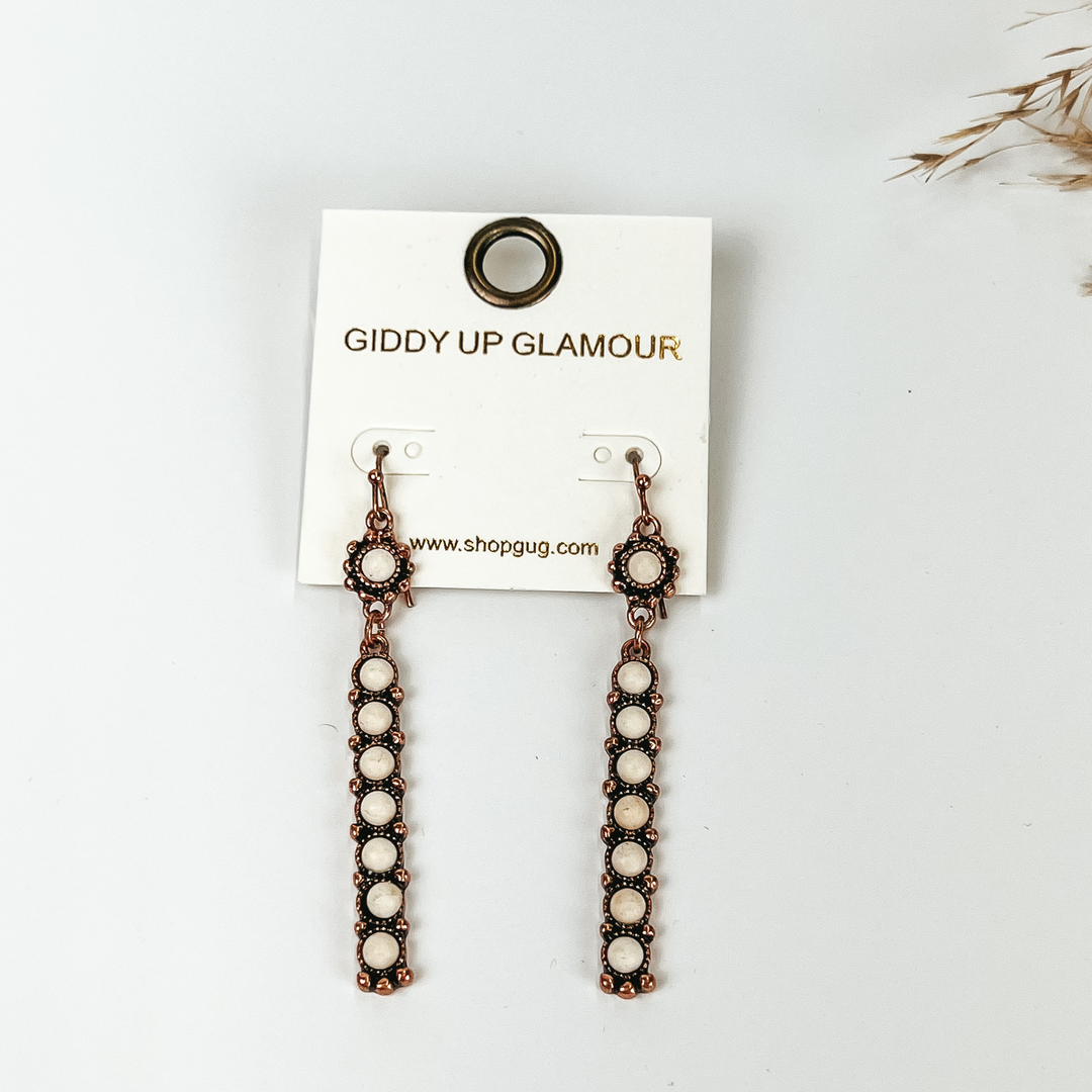 White cirle pendant copper tone rectangle bar earrings, with white stone pictured with pampas grass, on a white background. 