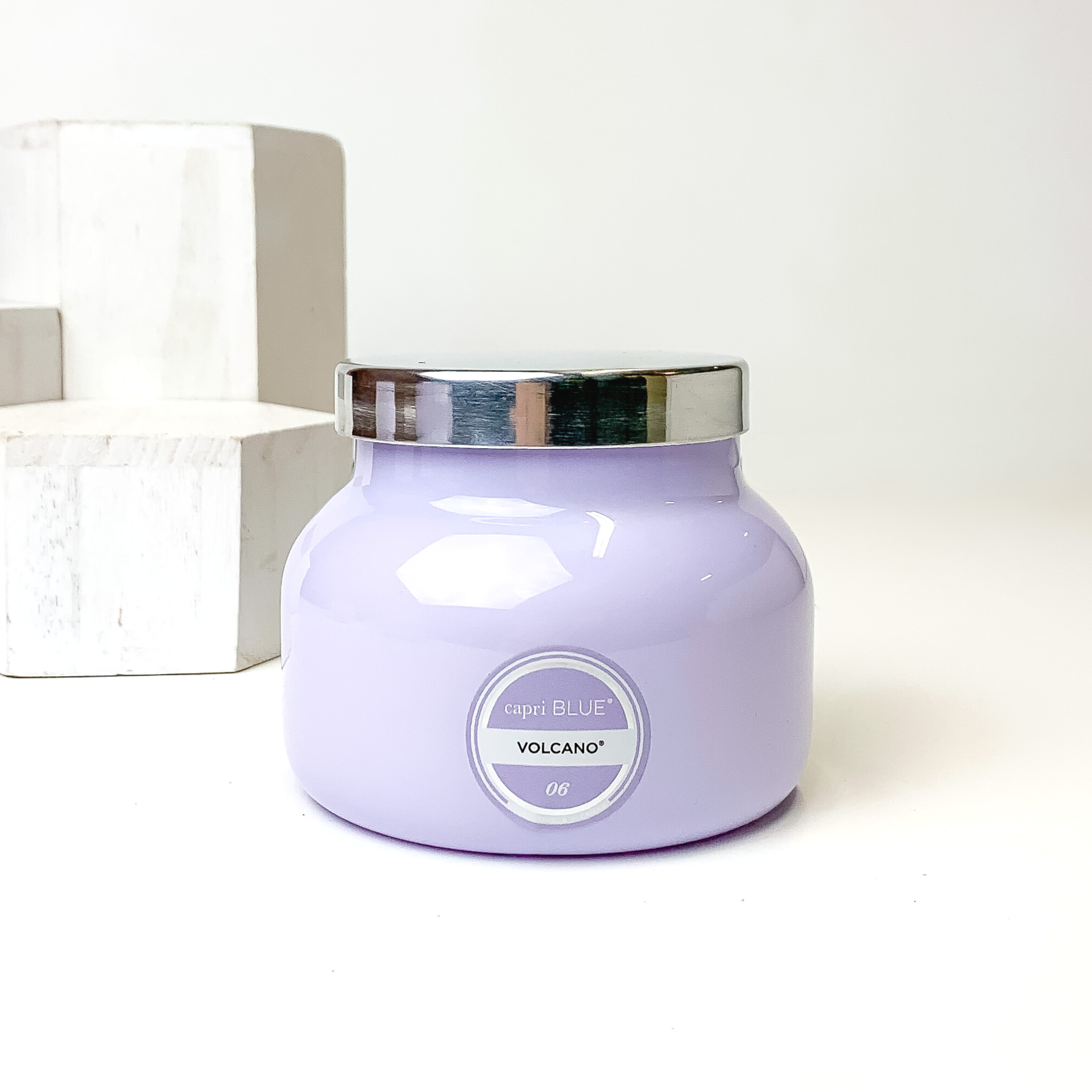 Light lavender candle with a silver lid. This candle is pictured on a white background with white blocks on the left side of the candle. 