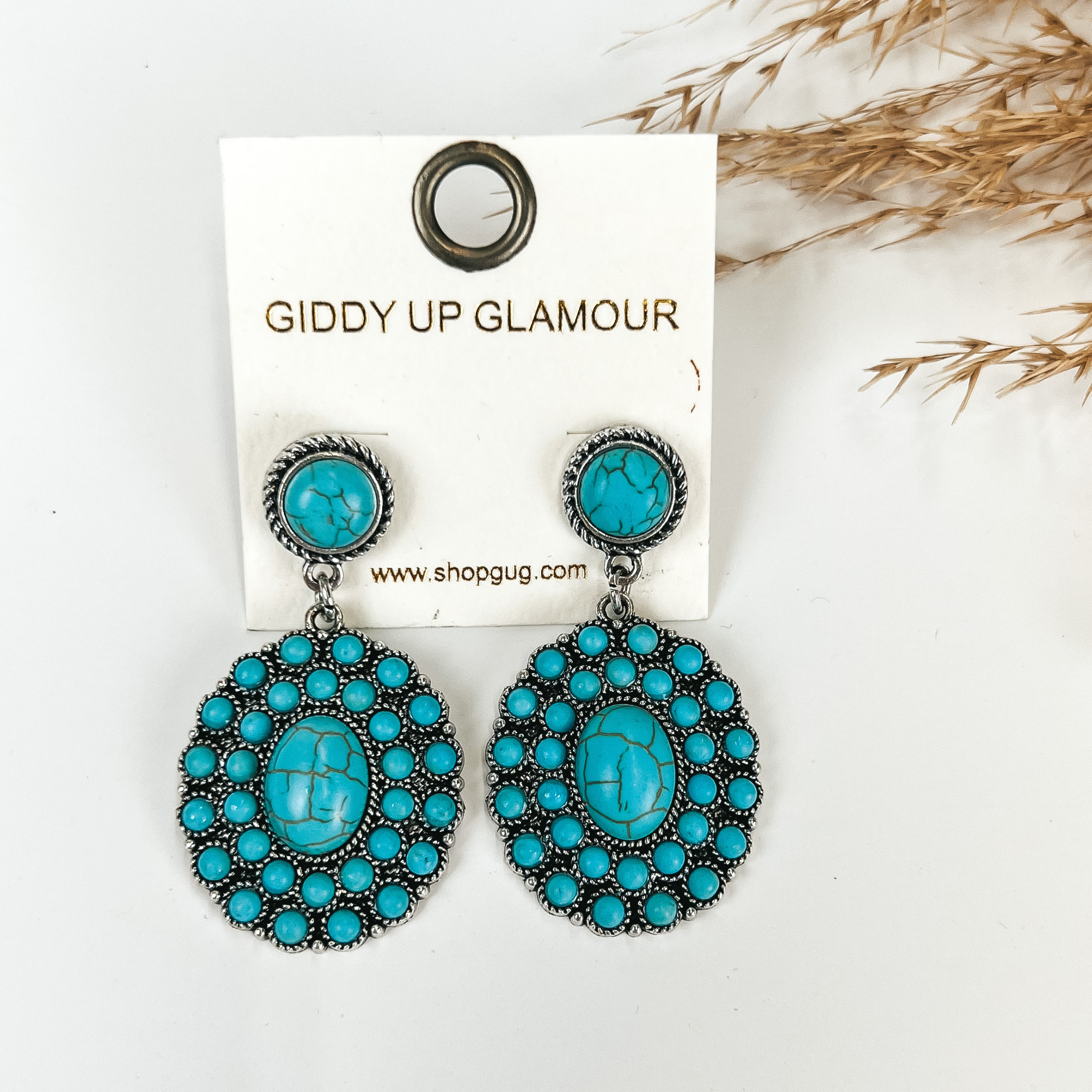 Turquoise circle post earrings with circle cluster drop with turquoise stones, pictured with pampas grass on a white background. 