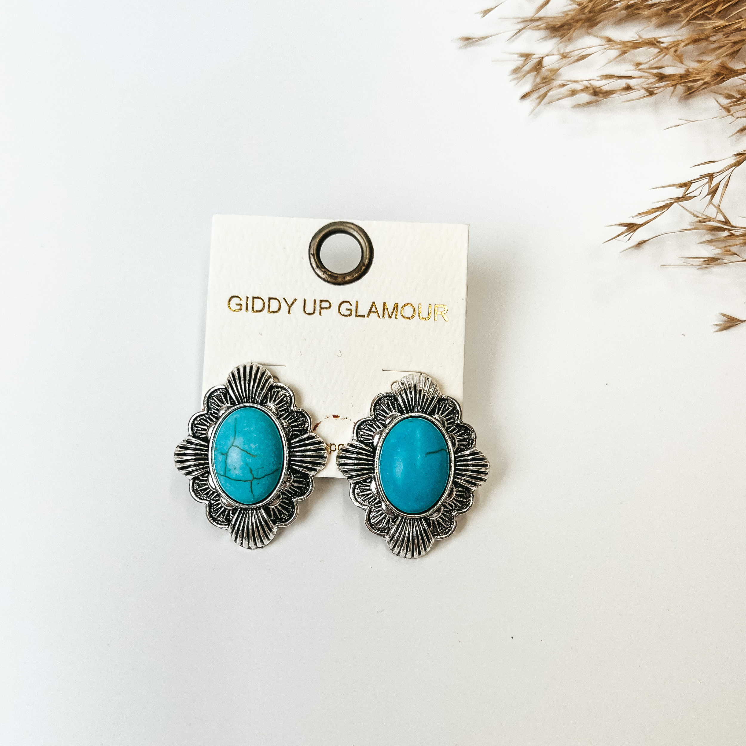 Silver tone post back earrings with oval stone in turquoise, pictured with pampas grass on a white background. 