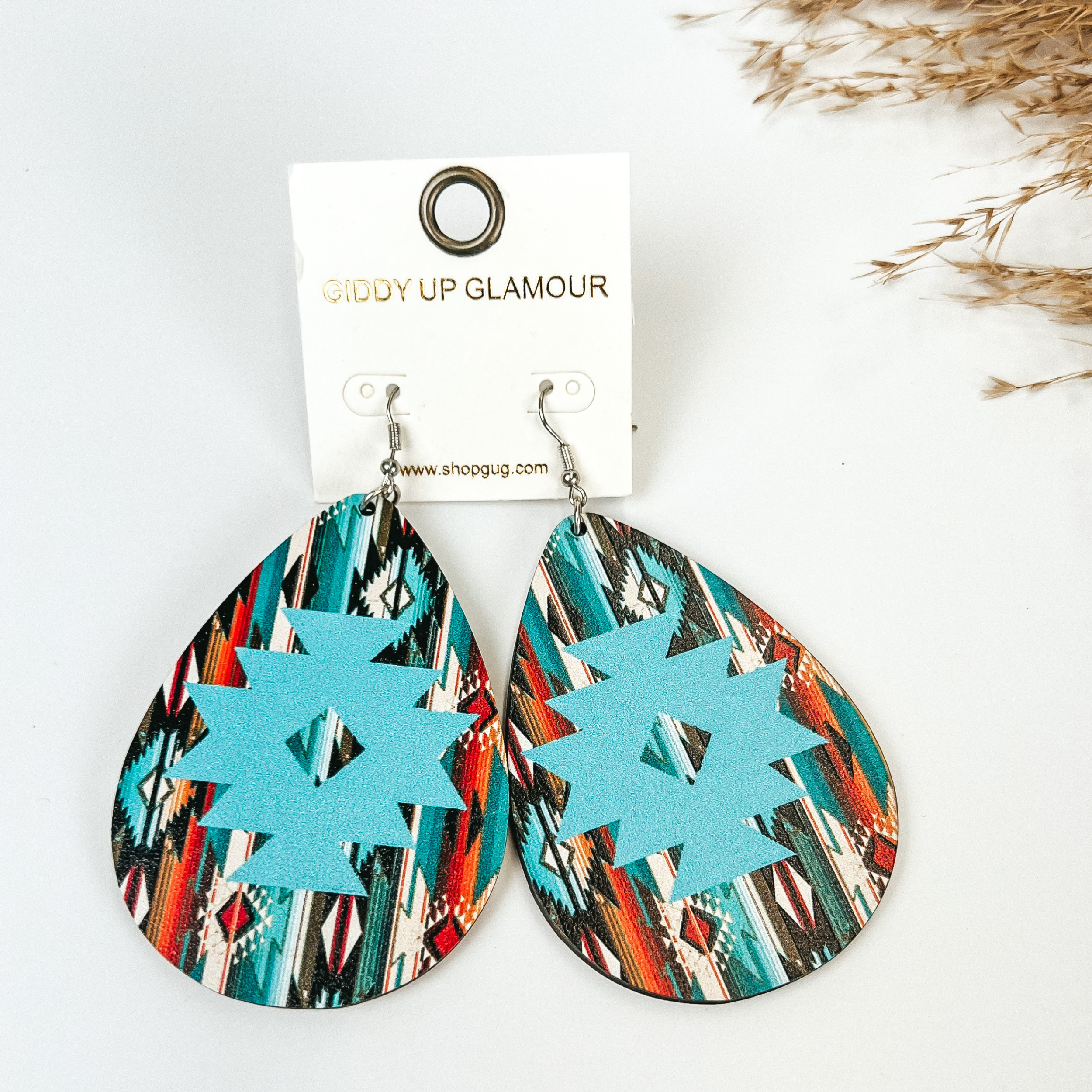 Wooden Serape teardrop earring with aztec print in Blue multicolor, pitcured with pampas grass on a white background. 