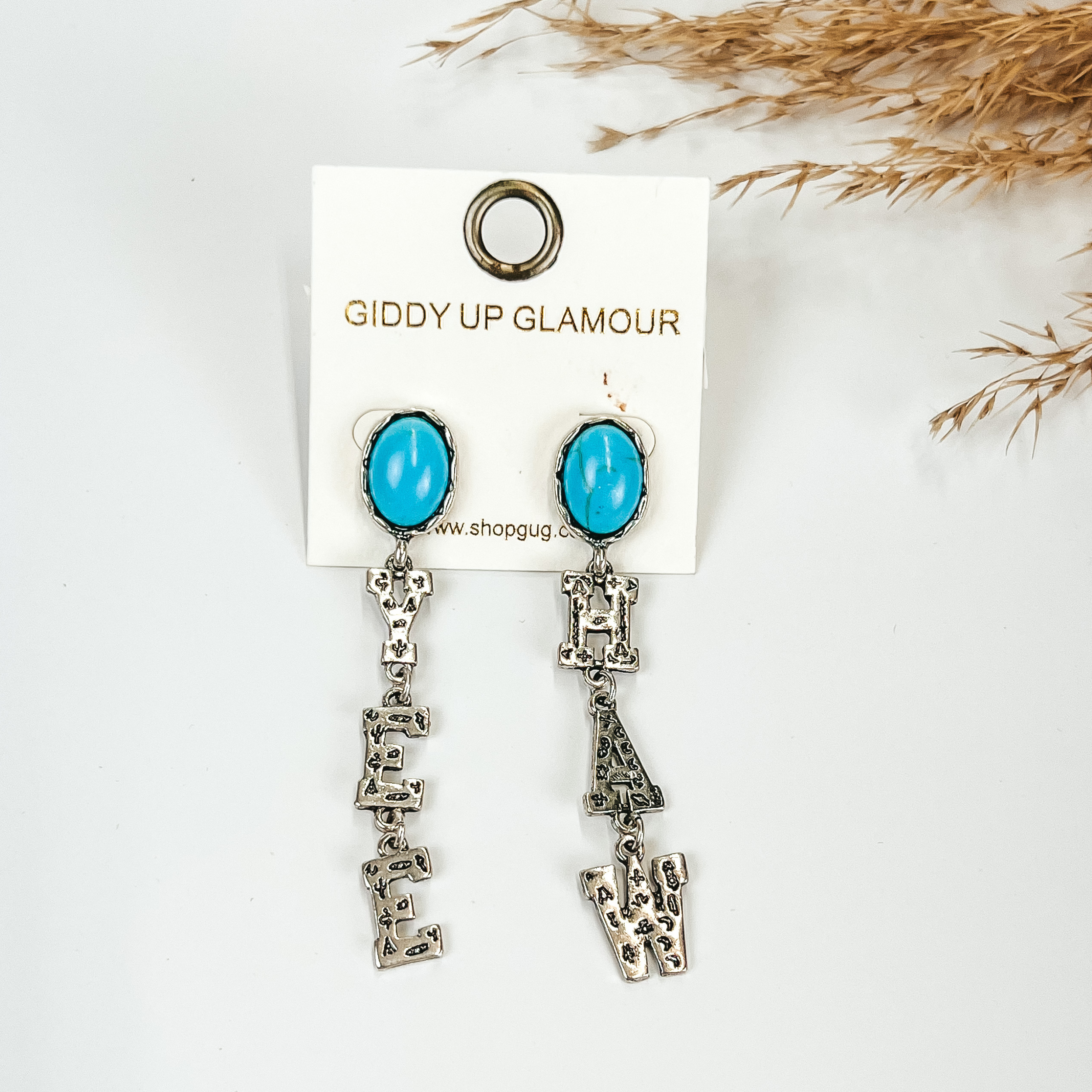 Yee Haw earrings in Silver tone with oval post back in turquoise, pictured with pampas grass, on a white background. 