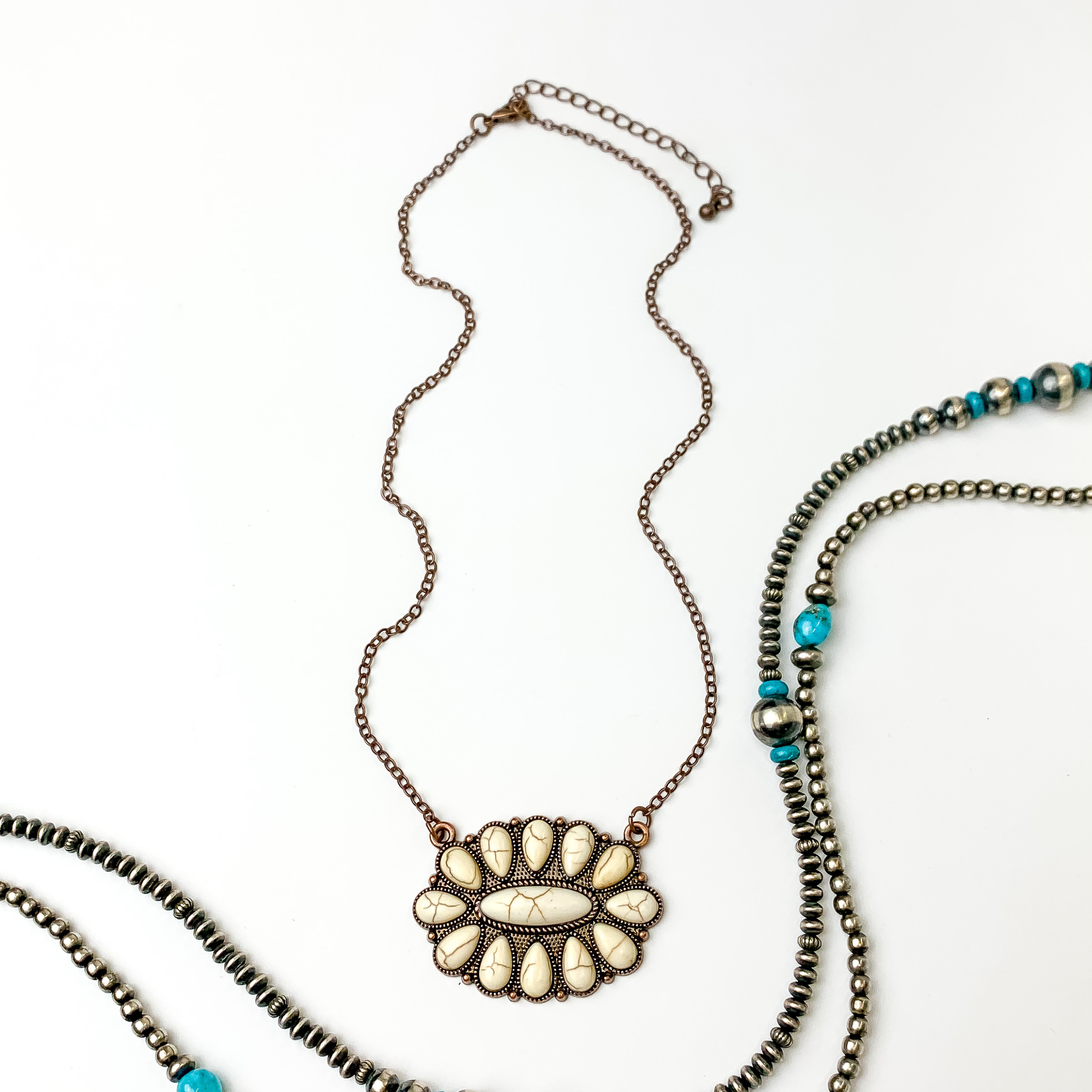 Copper chain necklace with oval cluster pendant. This pendant is made up of ivory stones. This necklace is pictured on an white background with silver and turquoise beads on the right side of the picture.