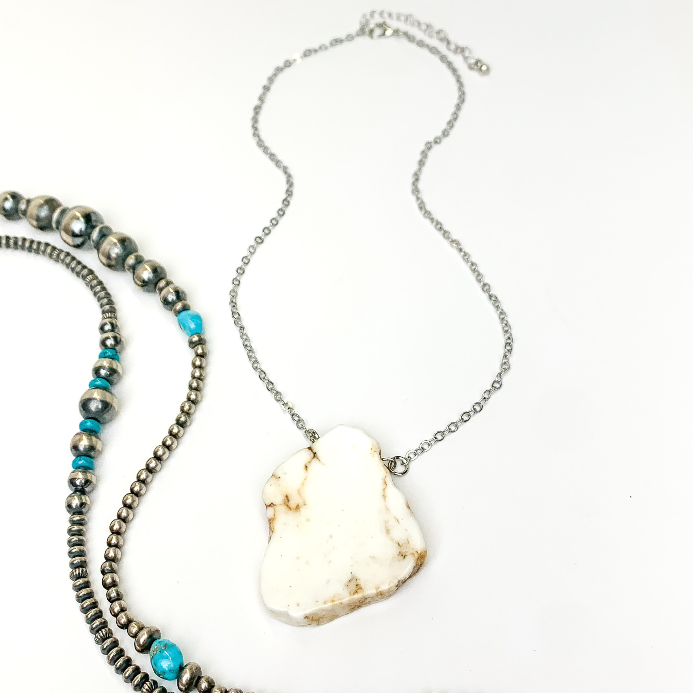 Silver chain necklace with ivory slab pendant. This necklace is pictured on an white background with silver and turquoise beads on the right side of the picture.