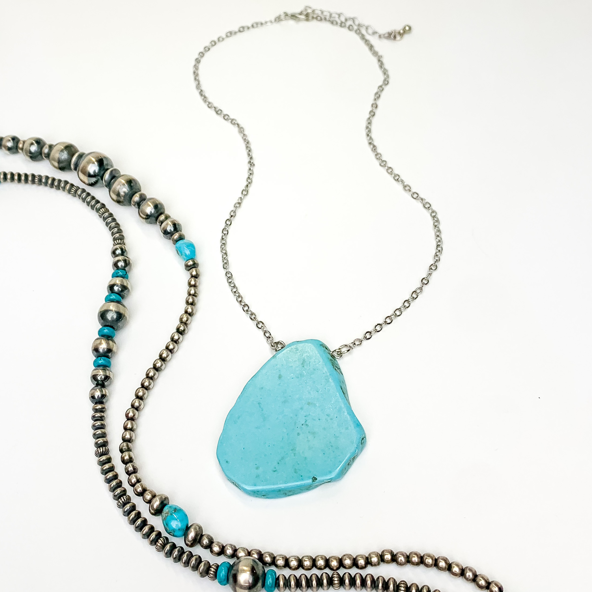 Silver chain necklace with turquoise slab pendant. This necklace is pictured on an white background with silver and turquoise beads on the right side of the picture.